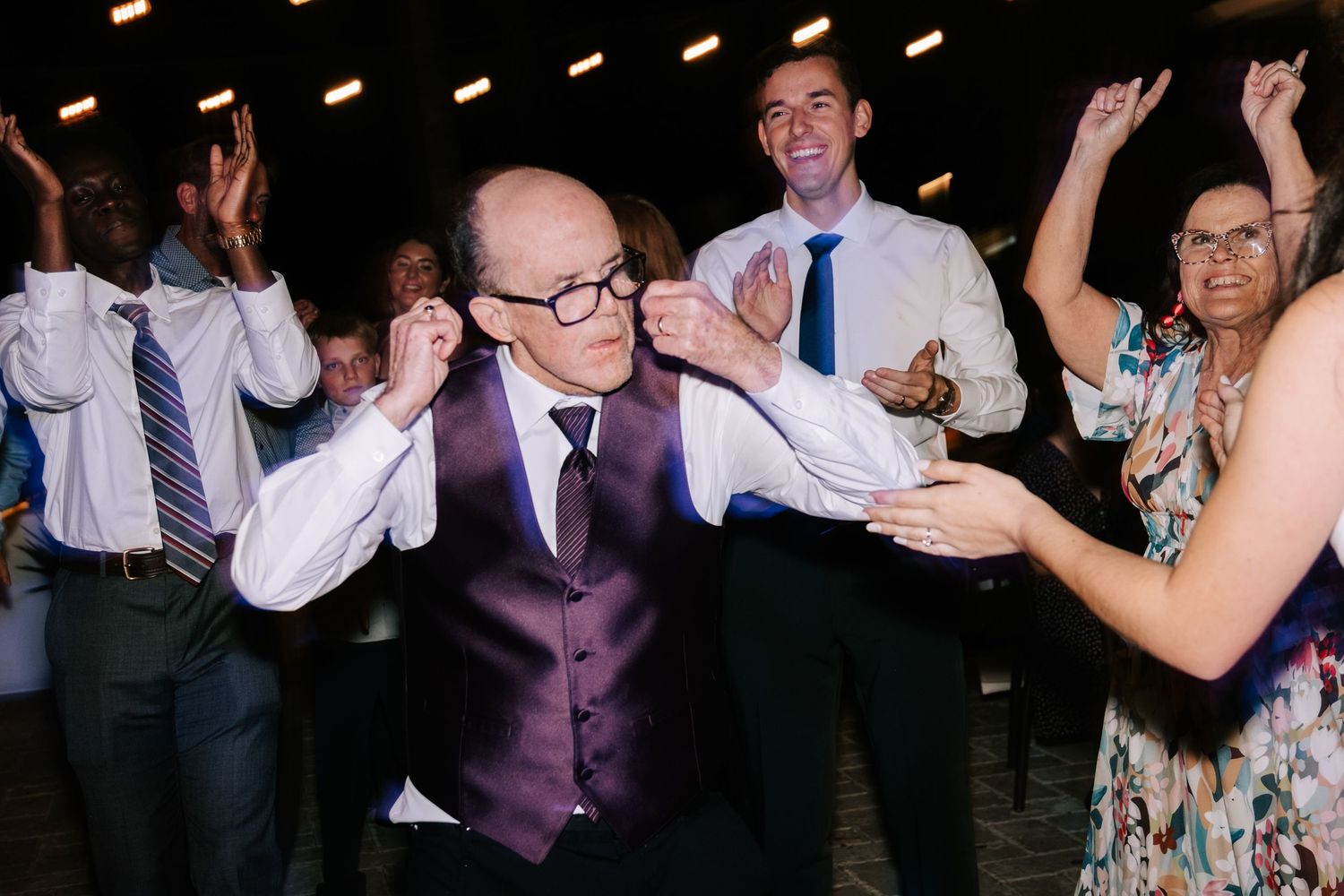 Wedding reception guests dancing and celebrating on a dark dance floor with ambient lighting.
