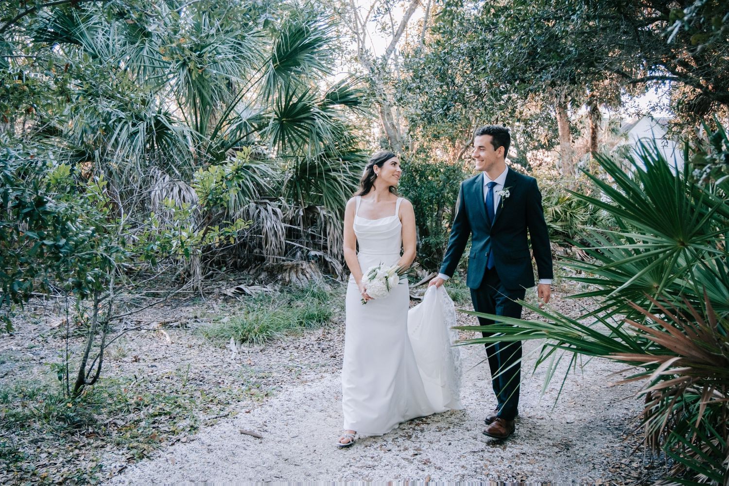 A couple walks along a path through tropical palm trees on their wedding day.