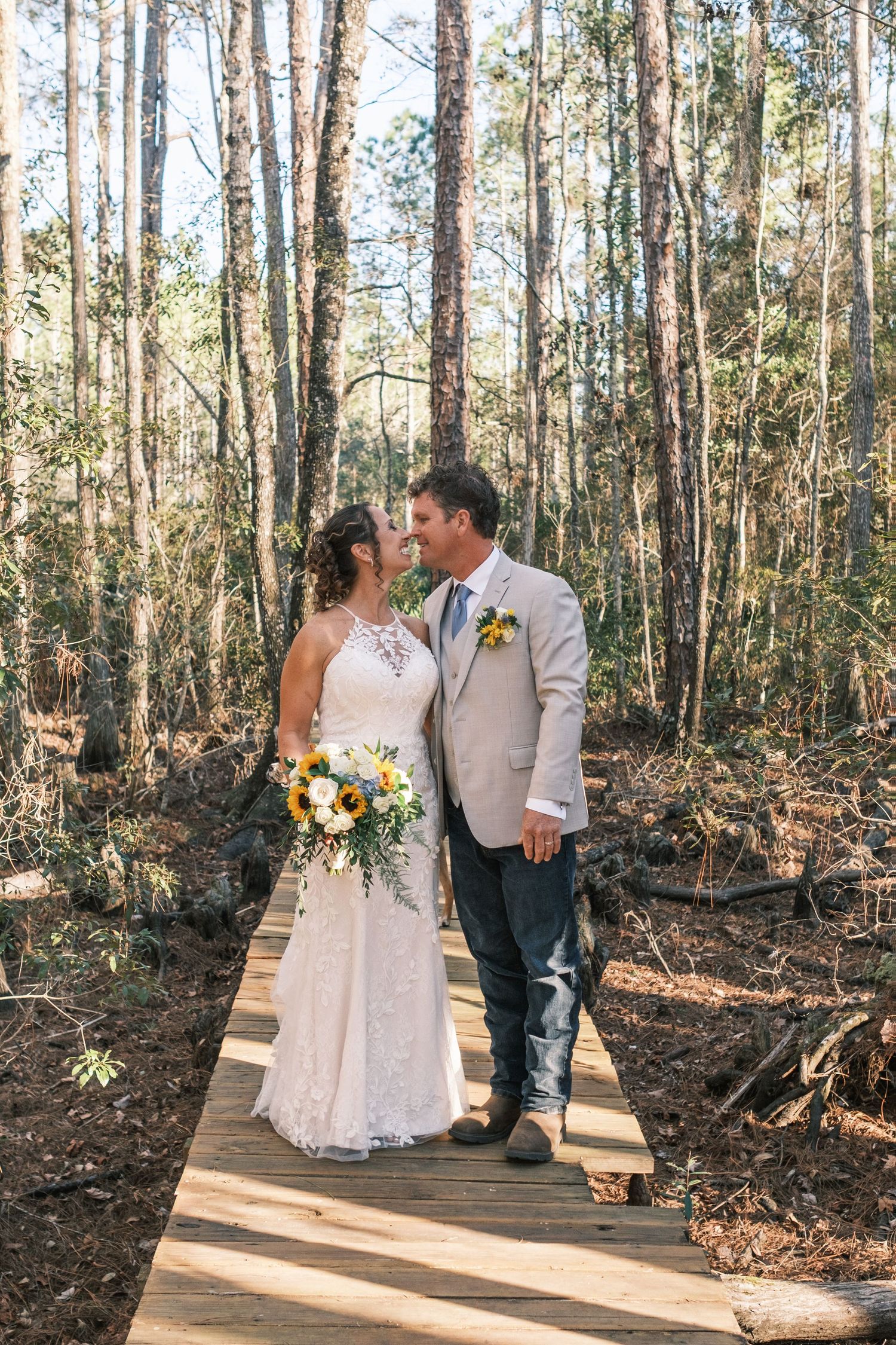 Bride and groom share a romantic moment on a wooden boardwalk surrounded by tall trees in a forest wedding.