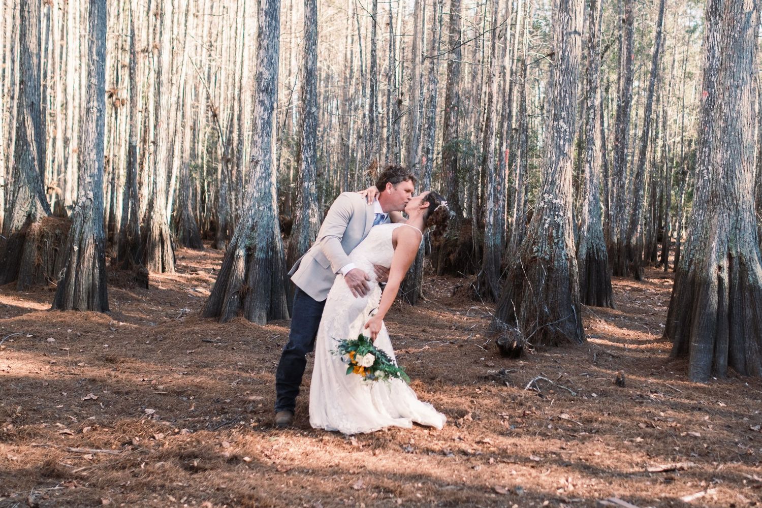 Groom dipping bride for a kiss in a wooded forest during wedding photo session.