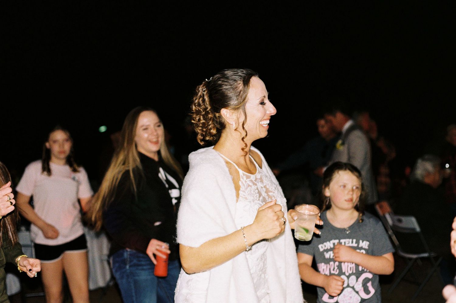 A bride in a white dress smiles while dancing at her outdoor evening wedding reception.