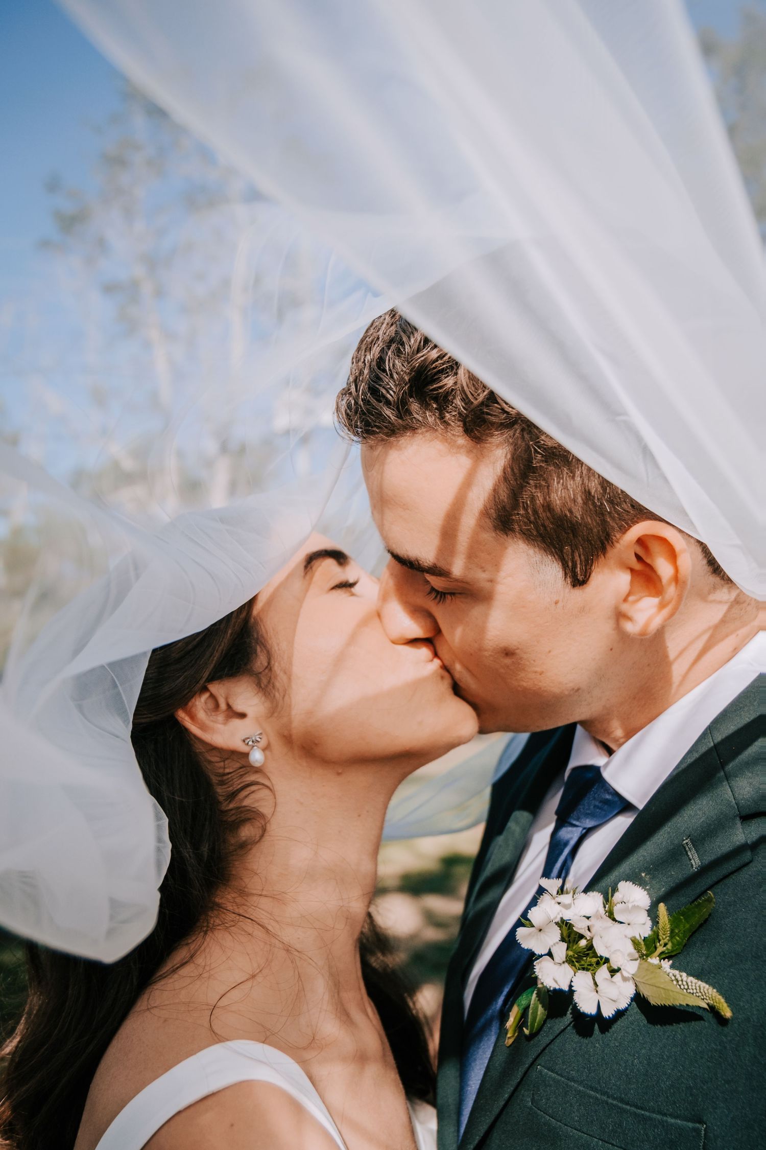 A romantic wedding kiss moment captured through a flowing white veil.