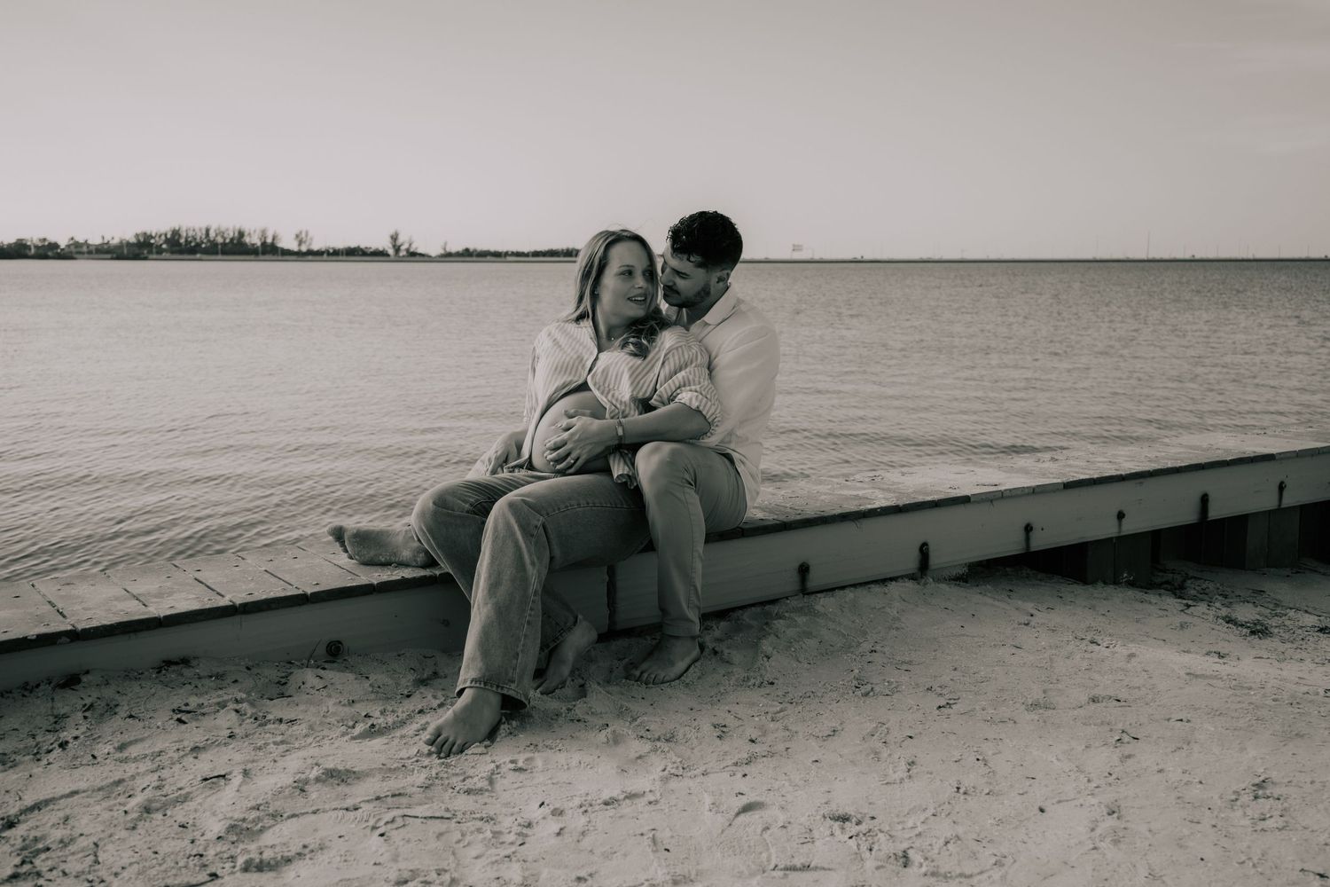 Black and white photo of people sitting on a dock by the water.