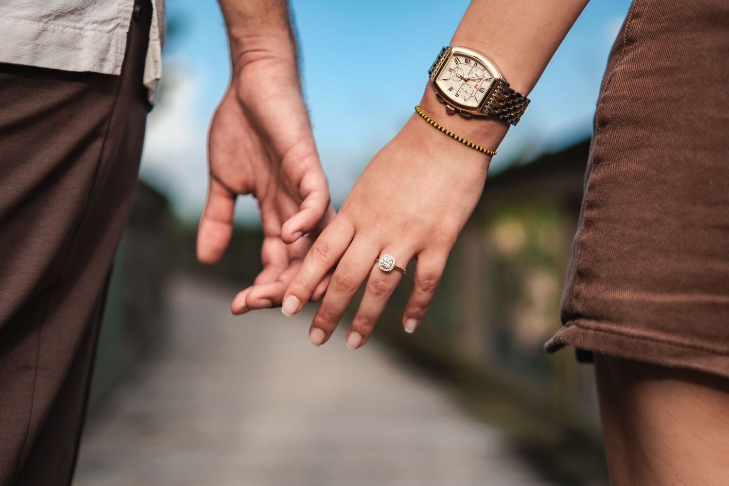 Detail shot of wedding rings and hands against blue sky background.