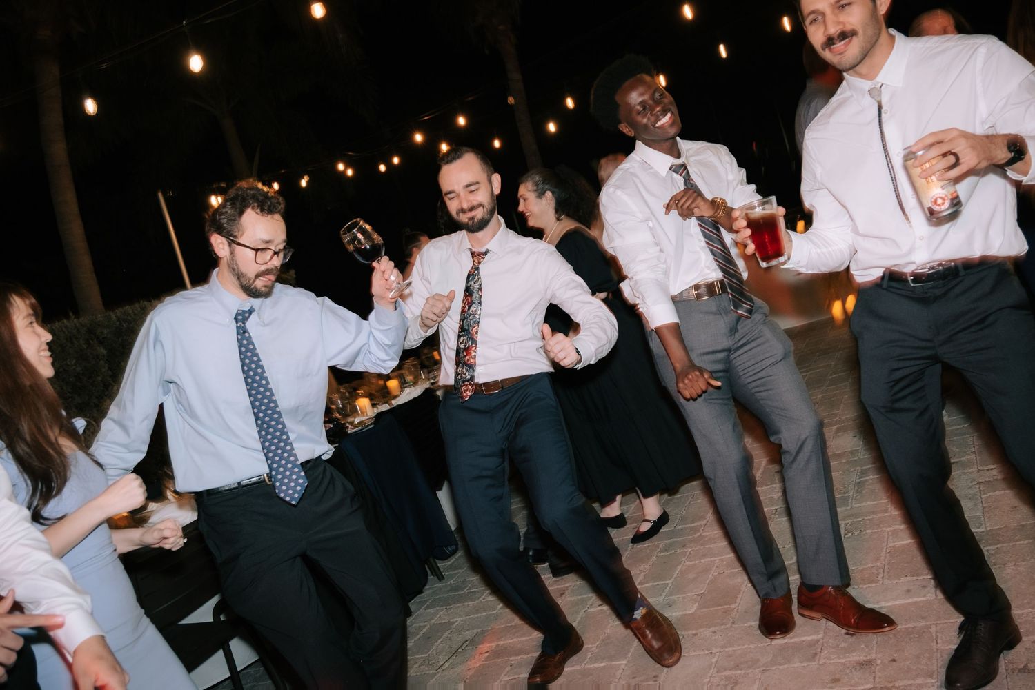Wedding guests dancing energetically on an outdoor dance floor at night.