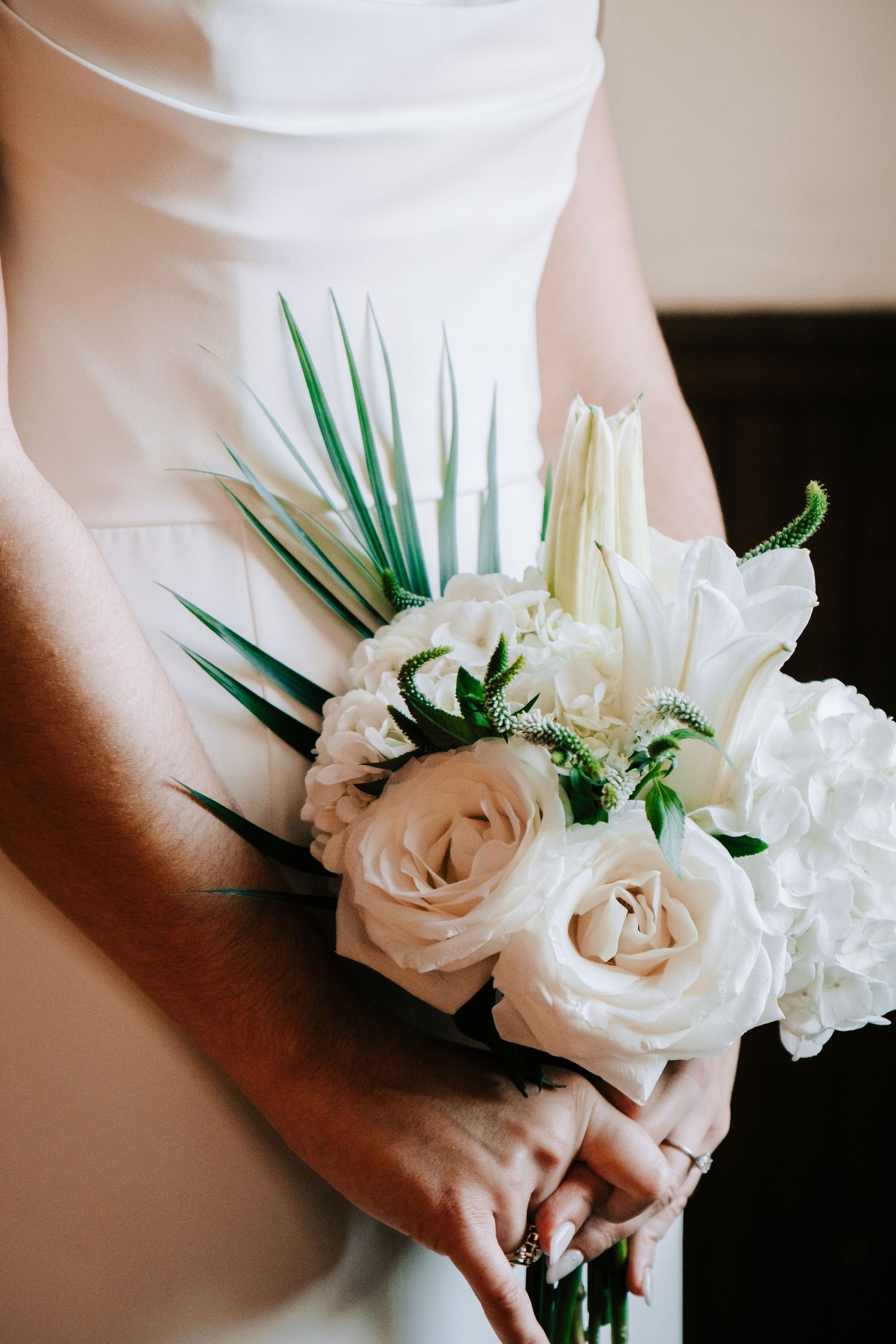 White roses and greenery arranged in an elegant bridal bouquet held against a light background.