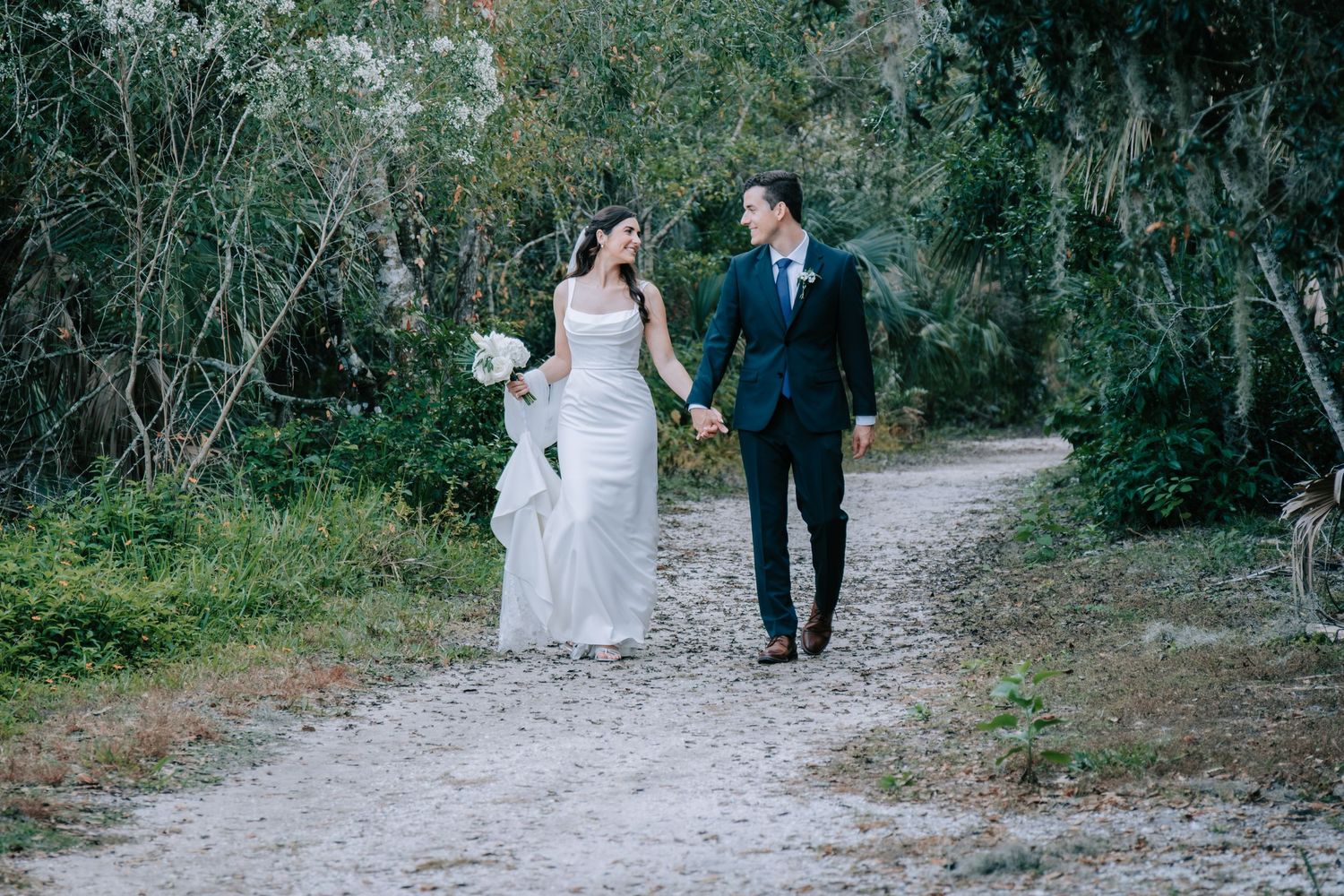 A couple walks along a scenic nature path during their wedding photoshoot.