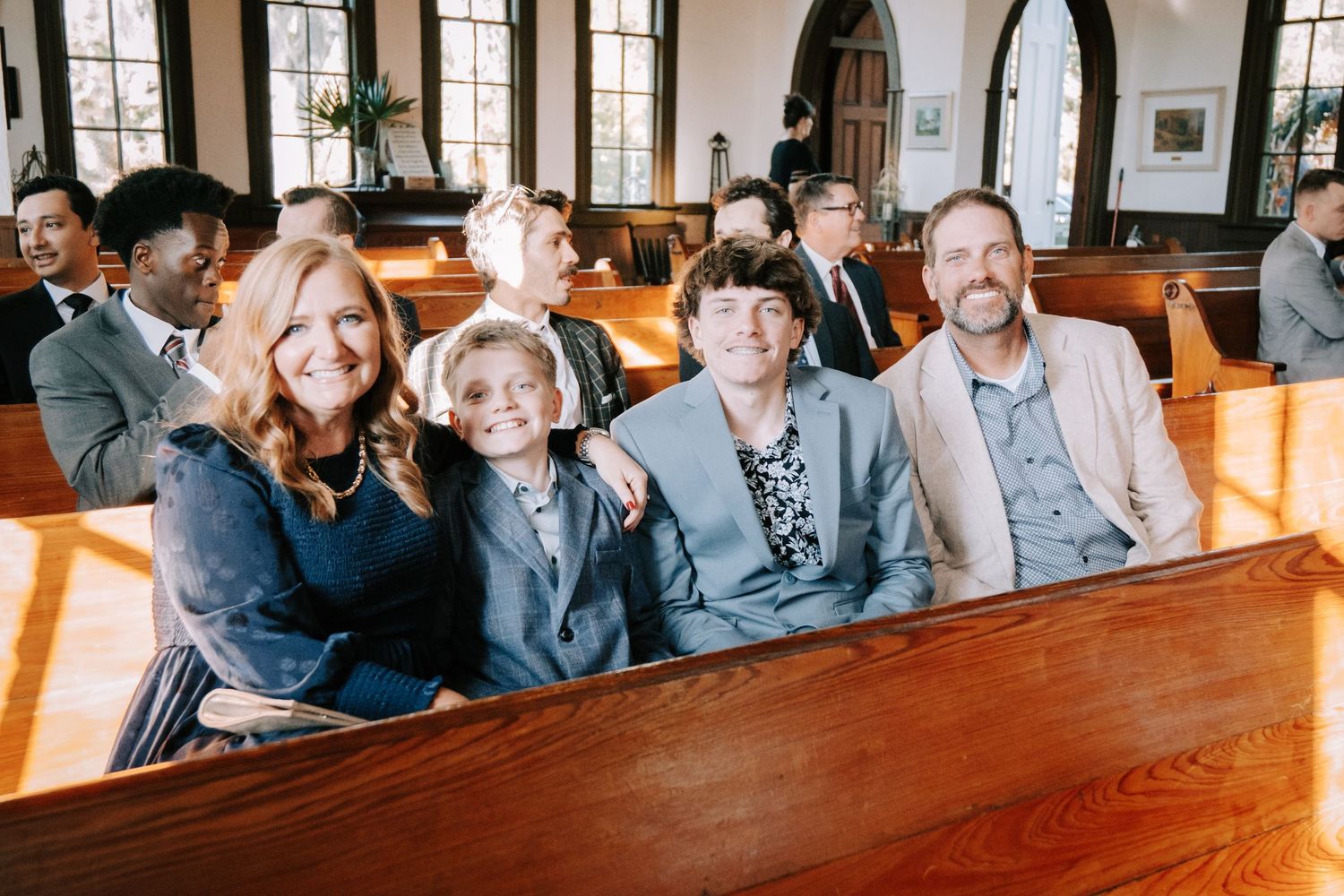A group sits together smiling and laughing in traditional wooden church pews during a service.