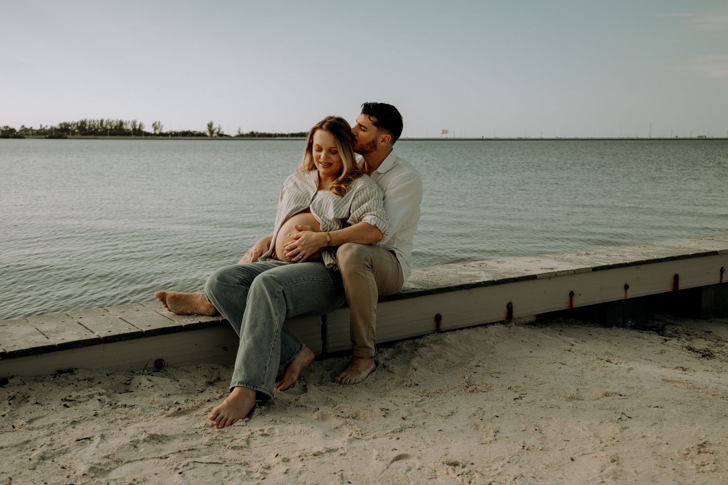 A couple sits together on a sandy beach at sunset enjoying a romantic moment by the water.