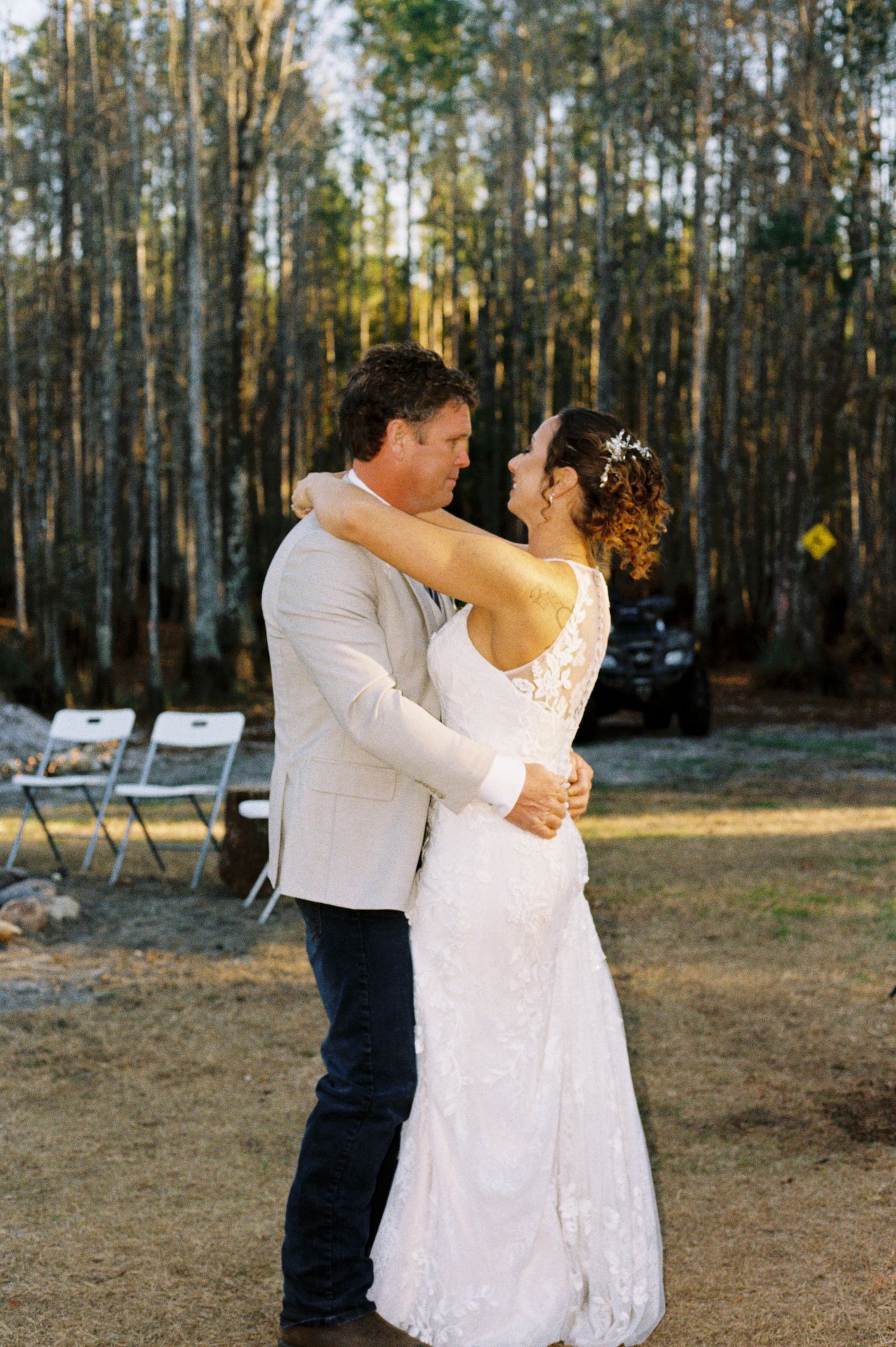 Bride and groom share first dance outdoors surrounded by pine trees at golden hour.