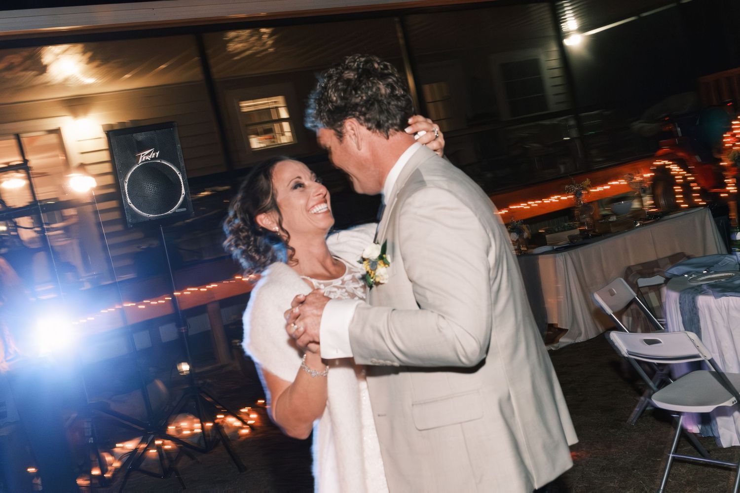 Bride and groom share their first dance on an outdoor patio illuminated by warm candlelight at their wedding reception.