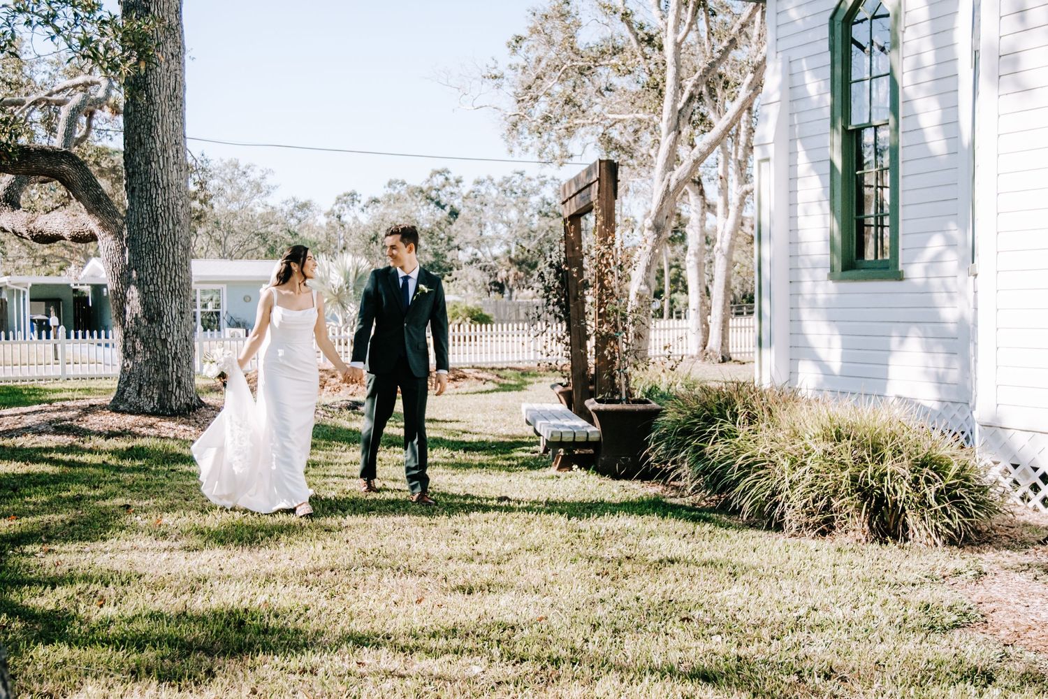 Newlyweds walk hand in hand on church grounds in sunlight.