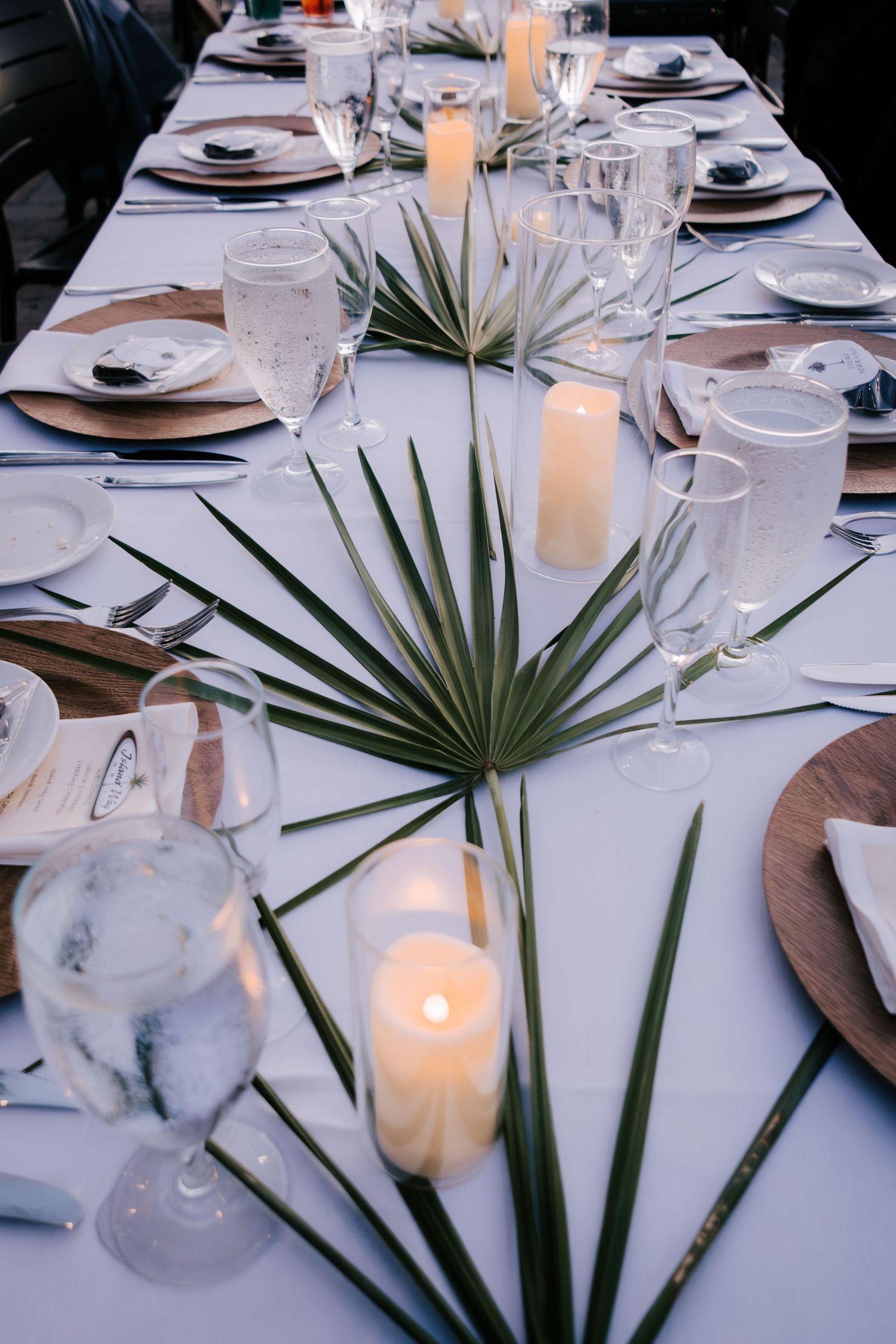 Elegant table settings with palm fronds and candles create a tropical wedding reception atmosphere.