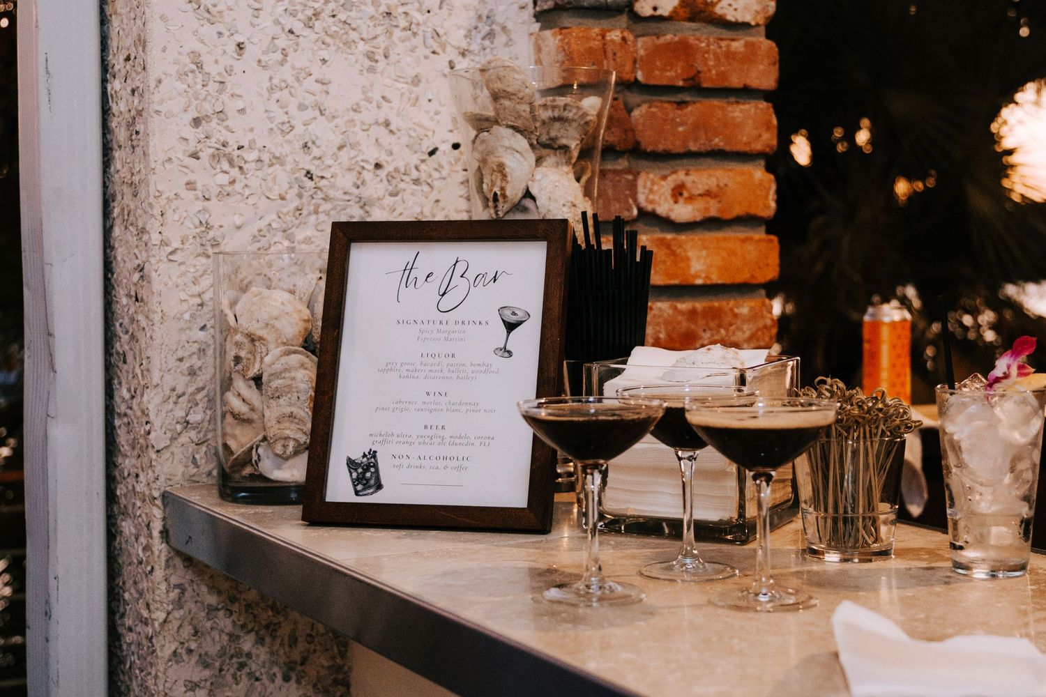 Reception table settings with brick wall backdrop and elegant glassware.