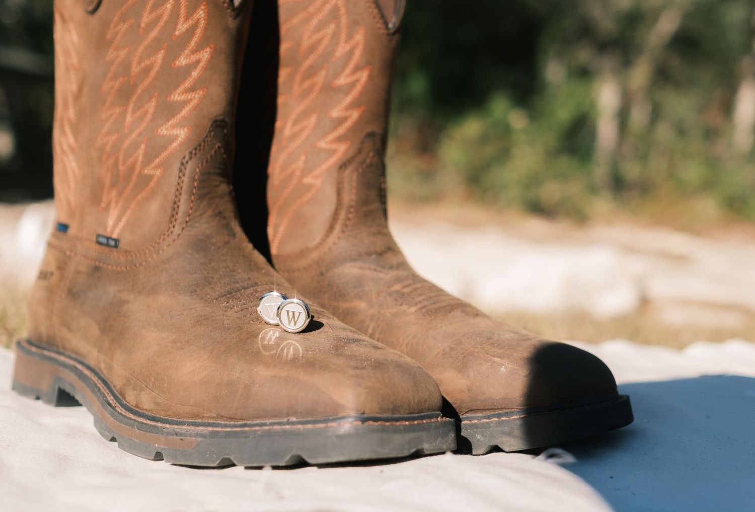 Close-up of worn brown cowboy boots with a wedding ring resting on top outdoors.