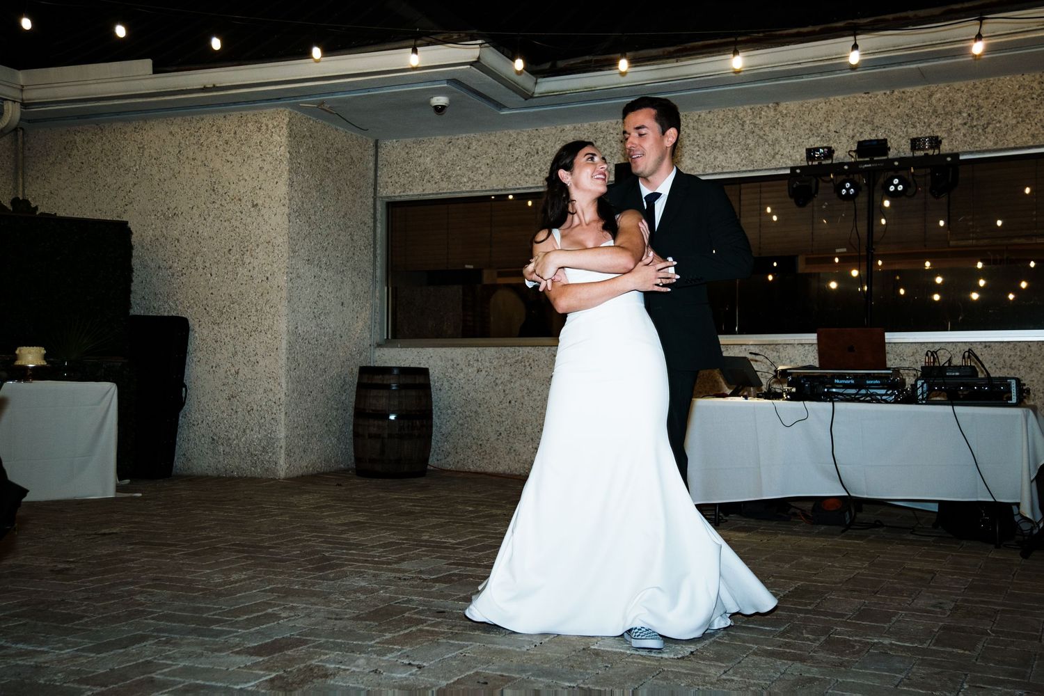 Wedding couple dancing in a dimly lit reception venue with string lights overhead.