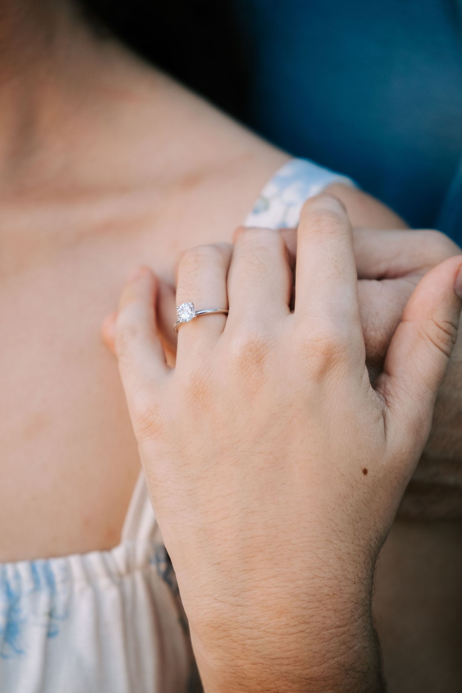 Close-up view of a diamond engagement ring on a woman's hand against a dark background.