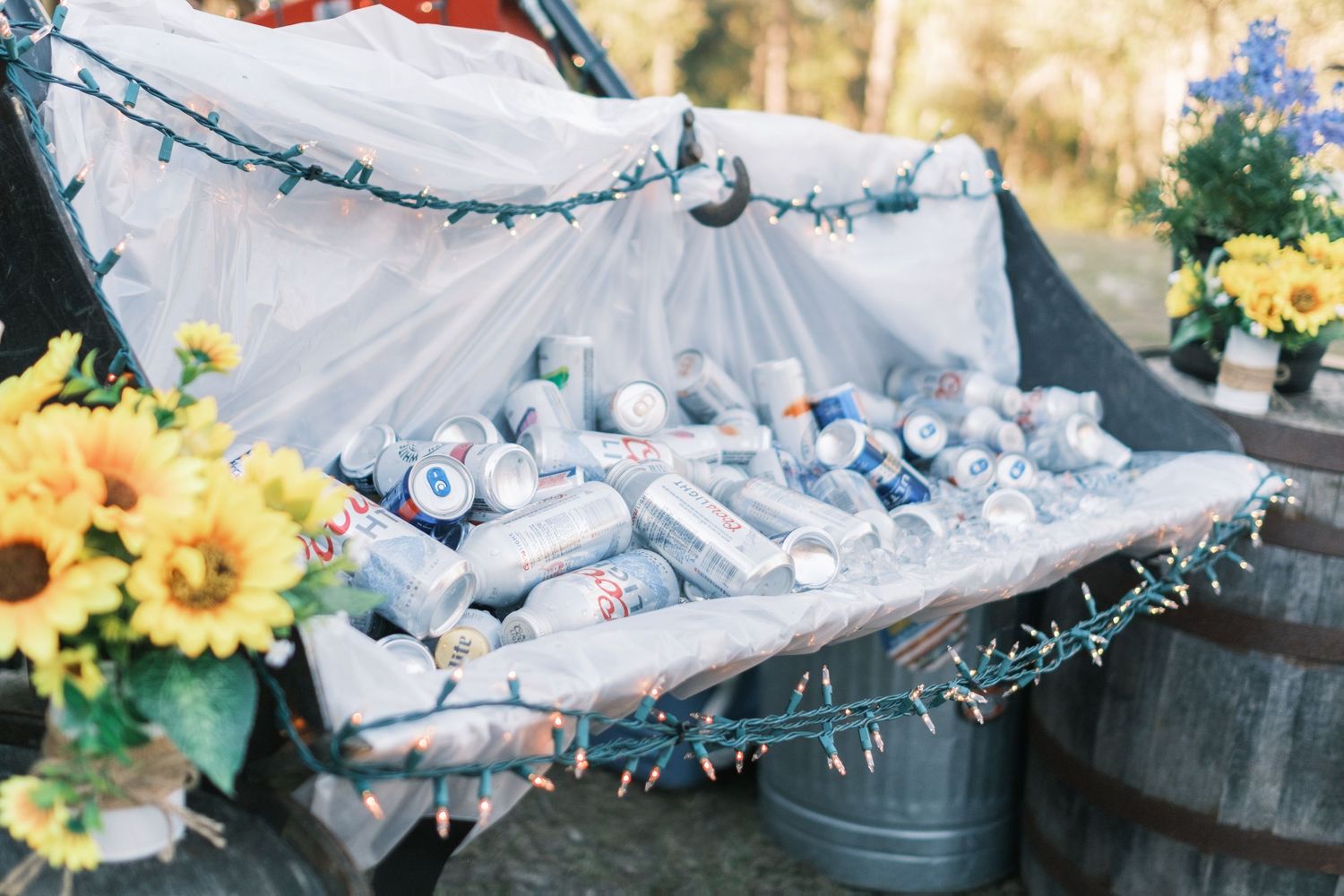 Truck bed filled with iced canned beverages decorated with string lights and sunflower arrangements.