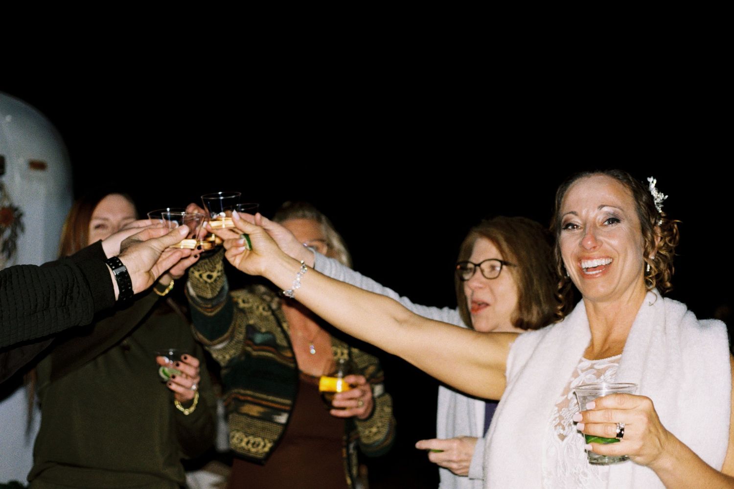 Bride smiles while raising sparklers with wedding guests during a joyful nighttime celebration toast.