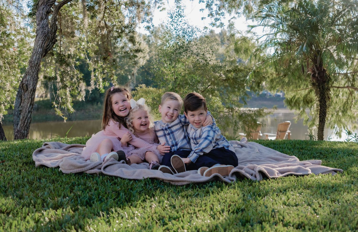 A group lies together on a blanket in a grassy park setting during a sunny day.
