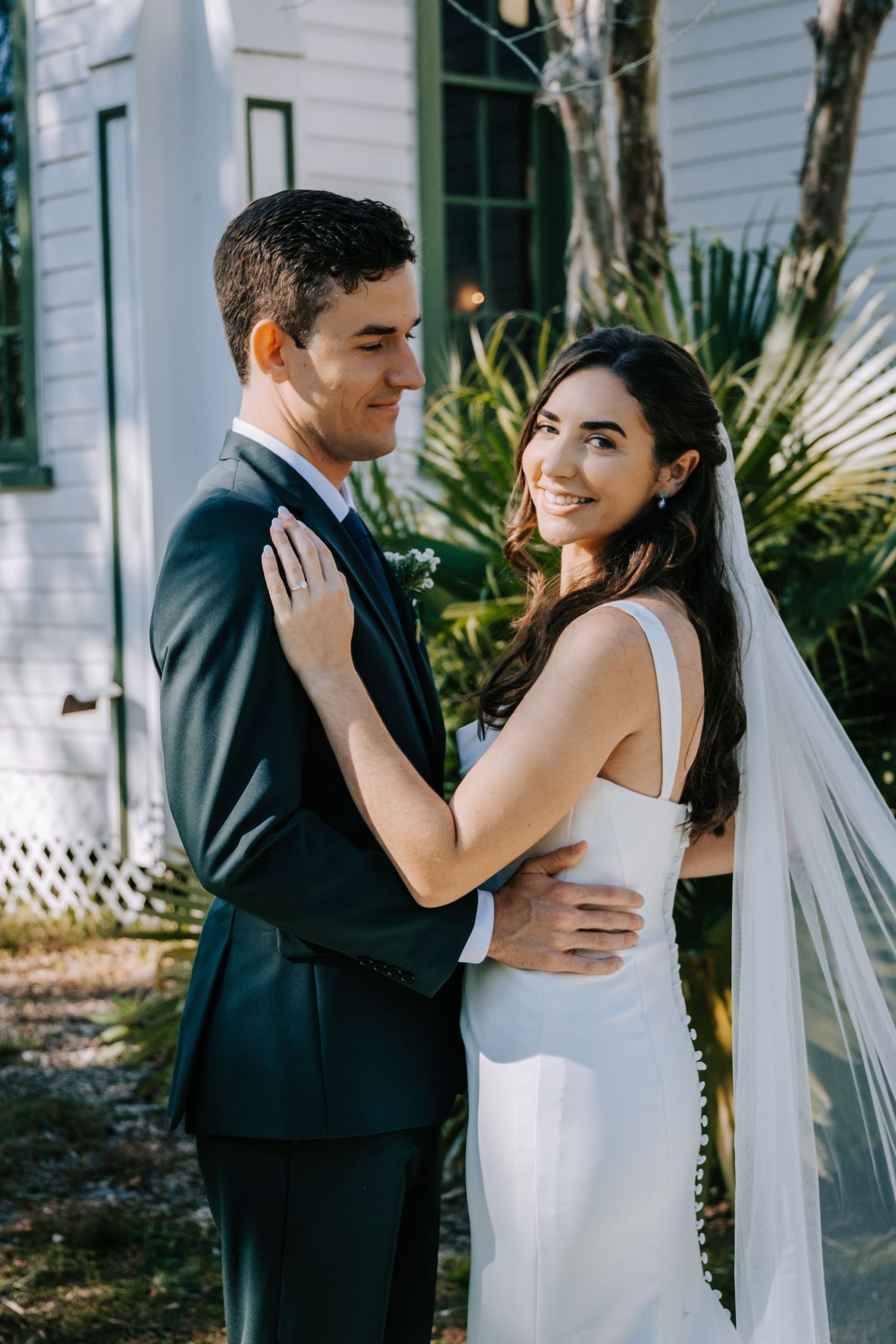 Romantic first look sequence between newlyweds outside a white historic building with palm trees.
