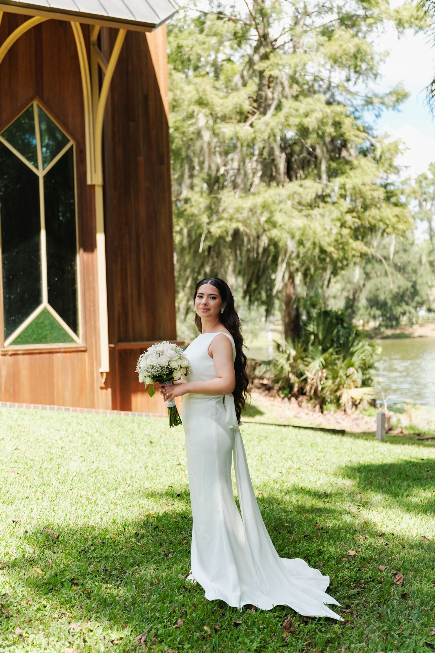 Elegant bridal portraits on a grassy lawn with a wooden gazebo and lake in the background.