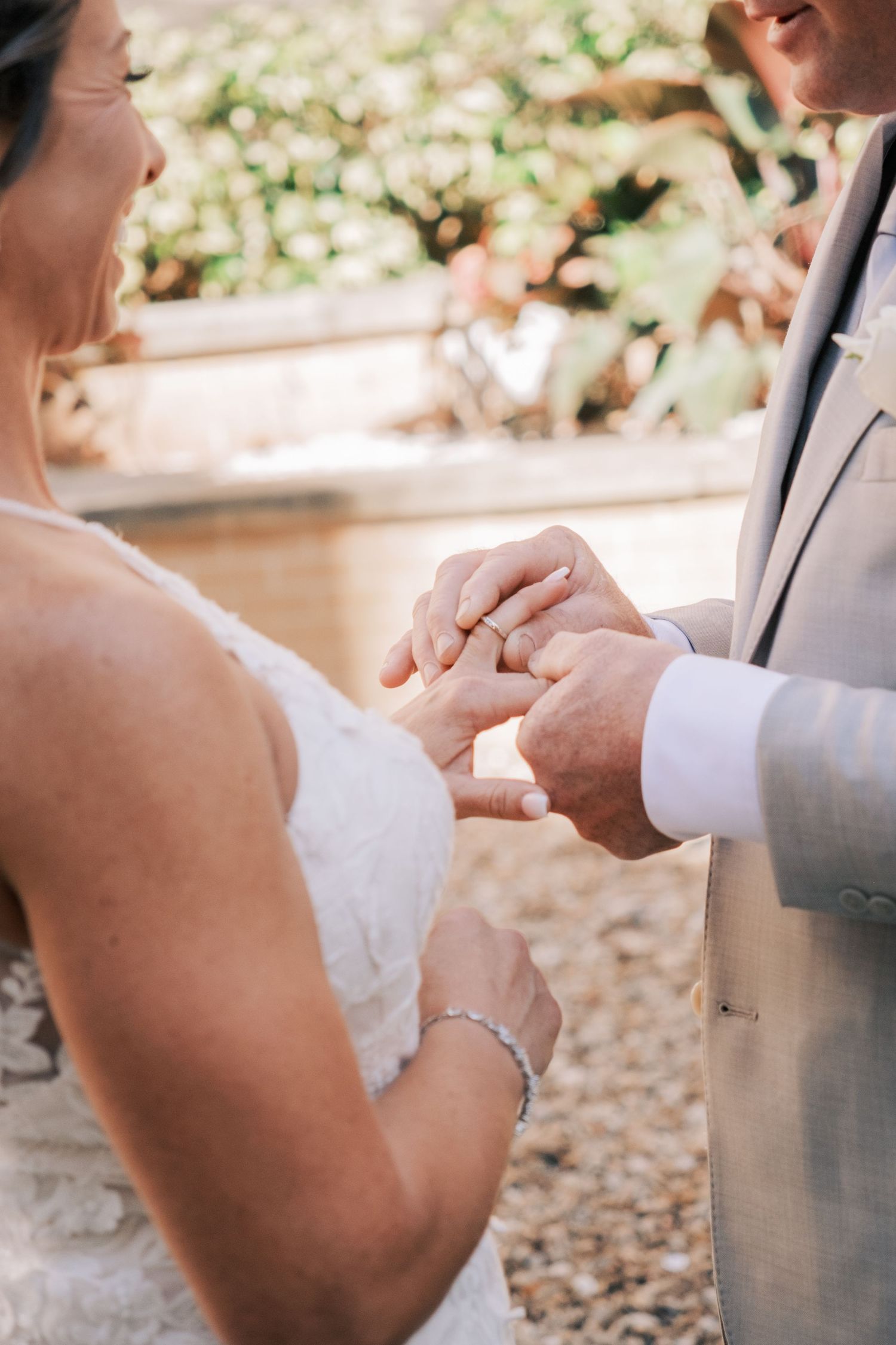 Groom places wedding ring on bride's finger during outdoor ring exchange ceremony.