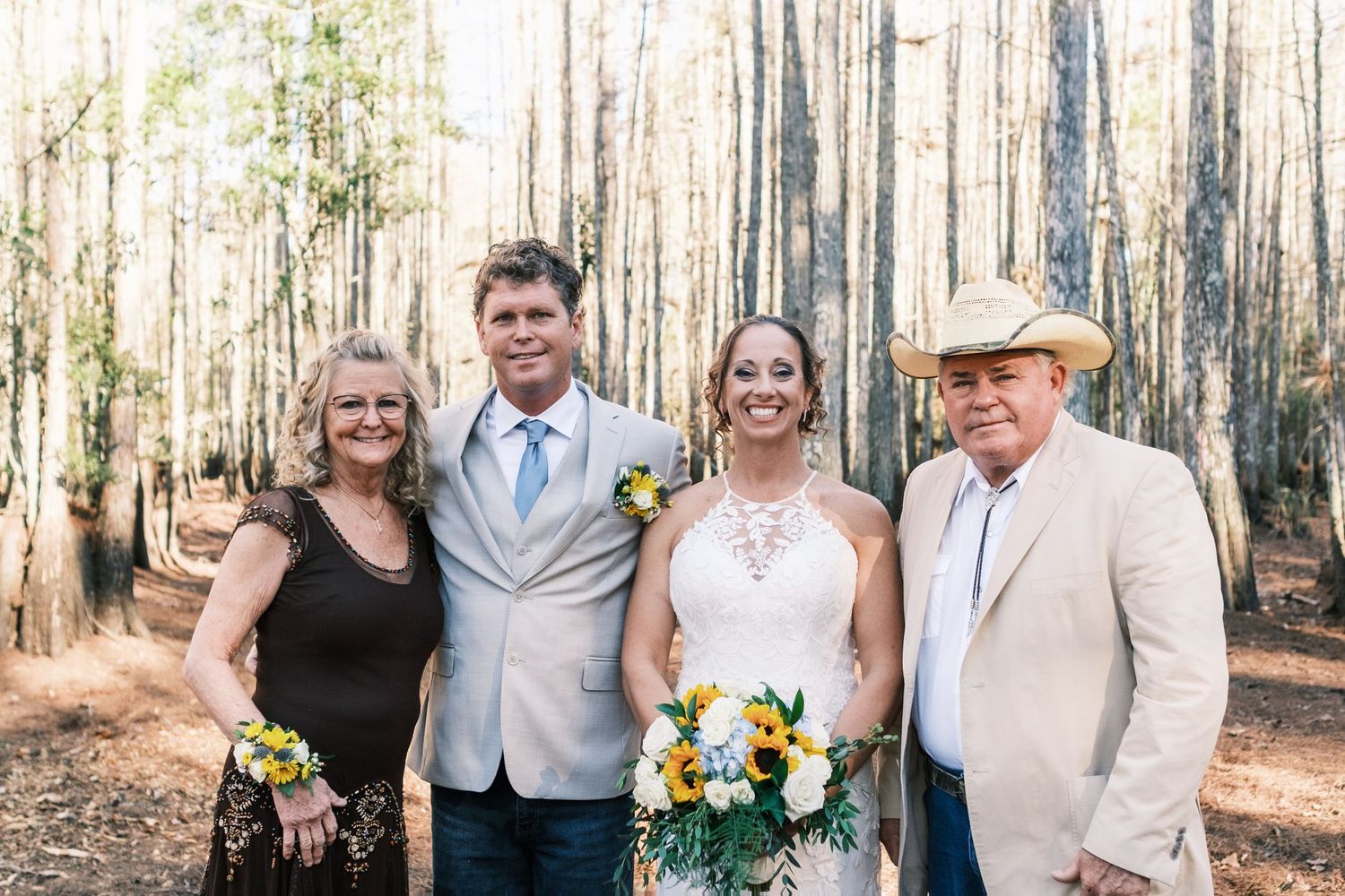 Wedding party of four smiles together in pine forest, man in cowboy hat on right.