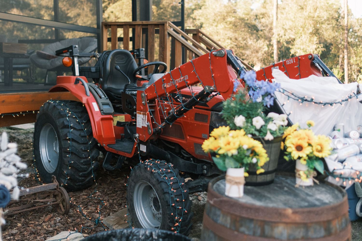 A red tractor displayed beside colorful flower arrangements at a rustic outdoor wedding venue.