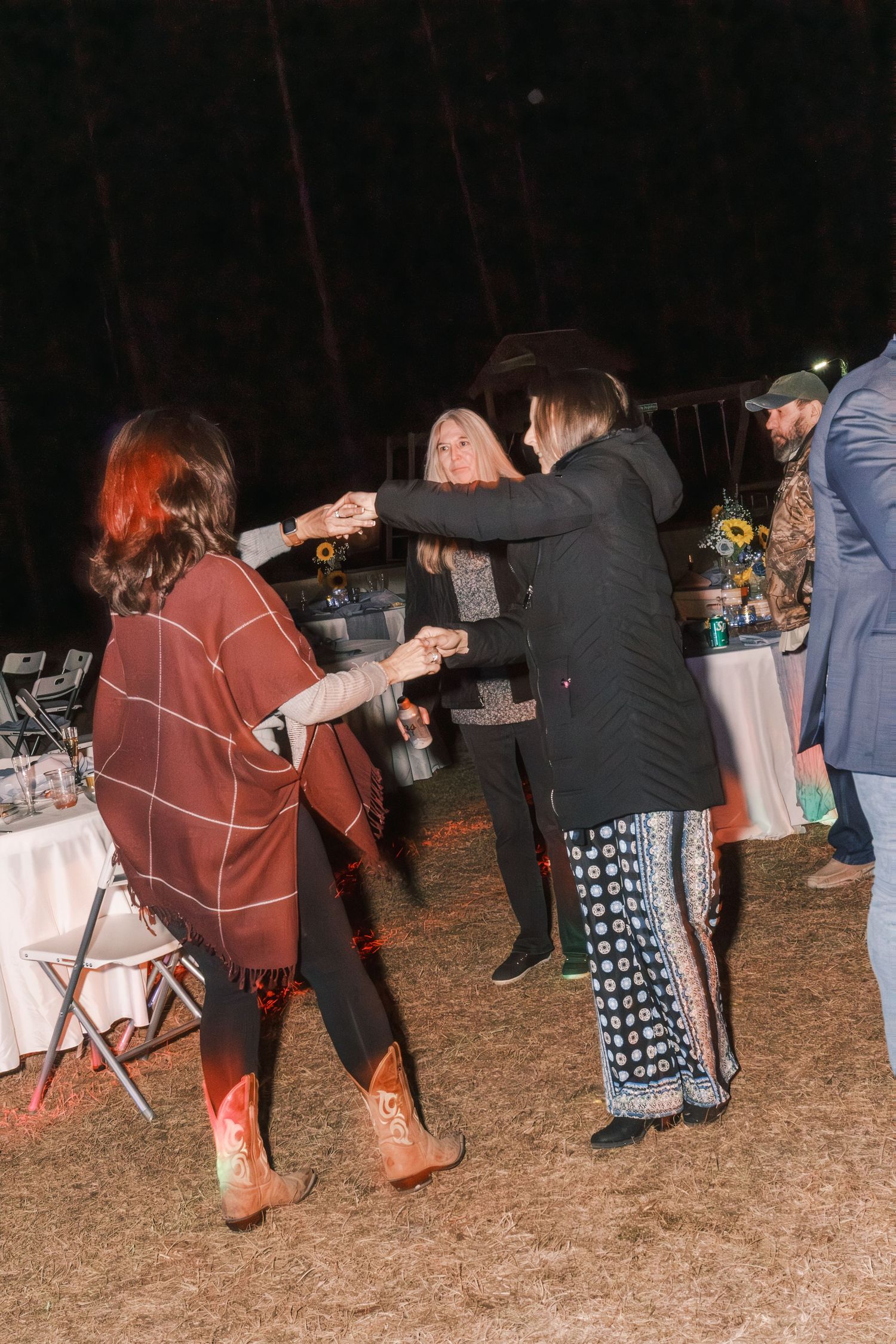 Guests dancing outdoors at night during a wedding reception surrounded by pine trees.