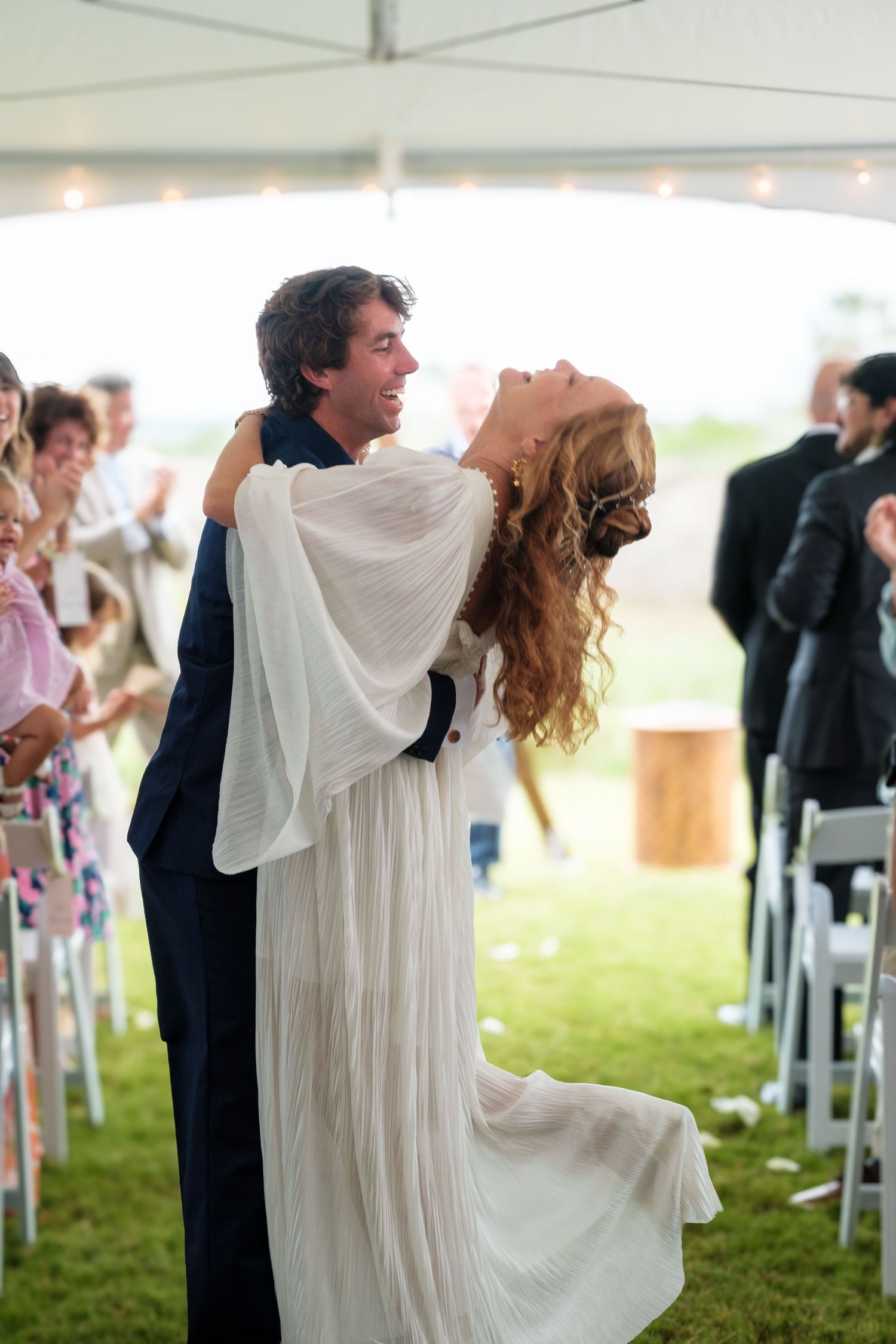 Dramatic wedding dance dip under white tent with guests seated in background.