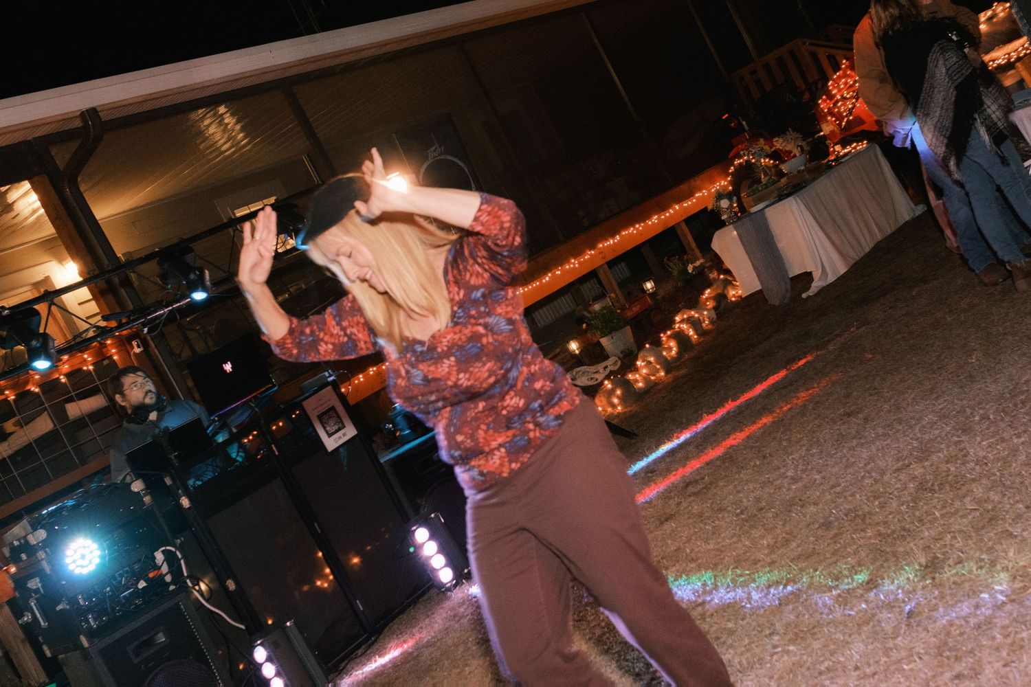 Guest in a floral outfit dancing energetically under colorful lights at an outdoor wedding reception.