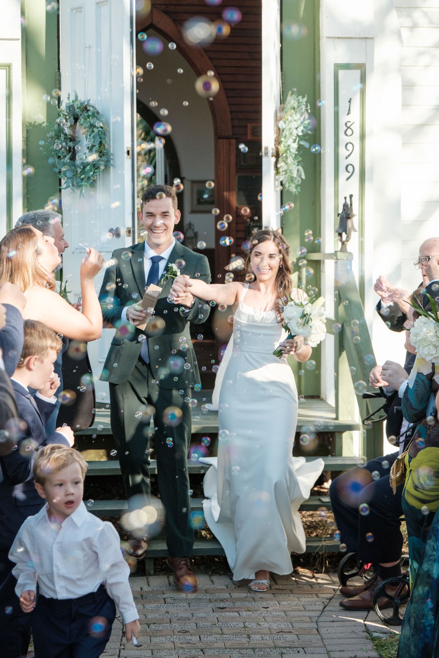 Wedding celebration with bubbles outside a historic building as guests cheer.