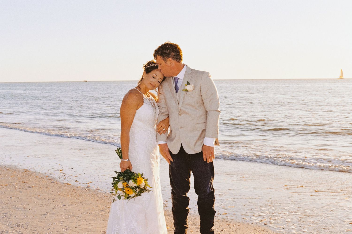 Bride and groom sharing a kiss on the beach at golden hour sunset.