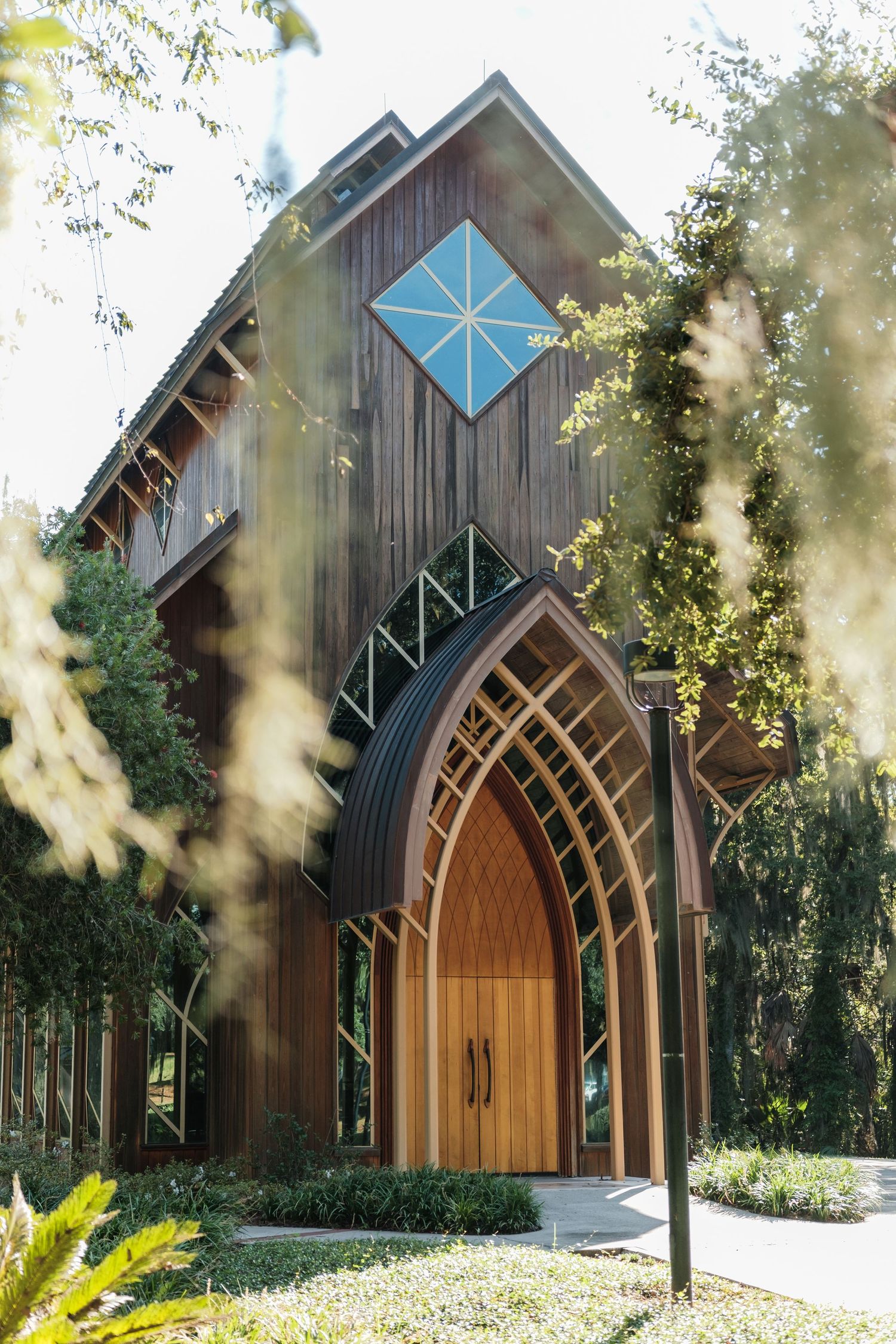 Modern wooden chapel with distinctive arched doorway and blue diamond window feature in natural setting.