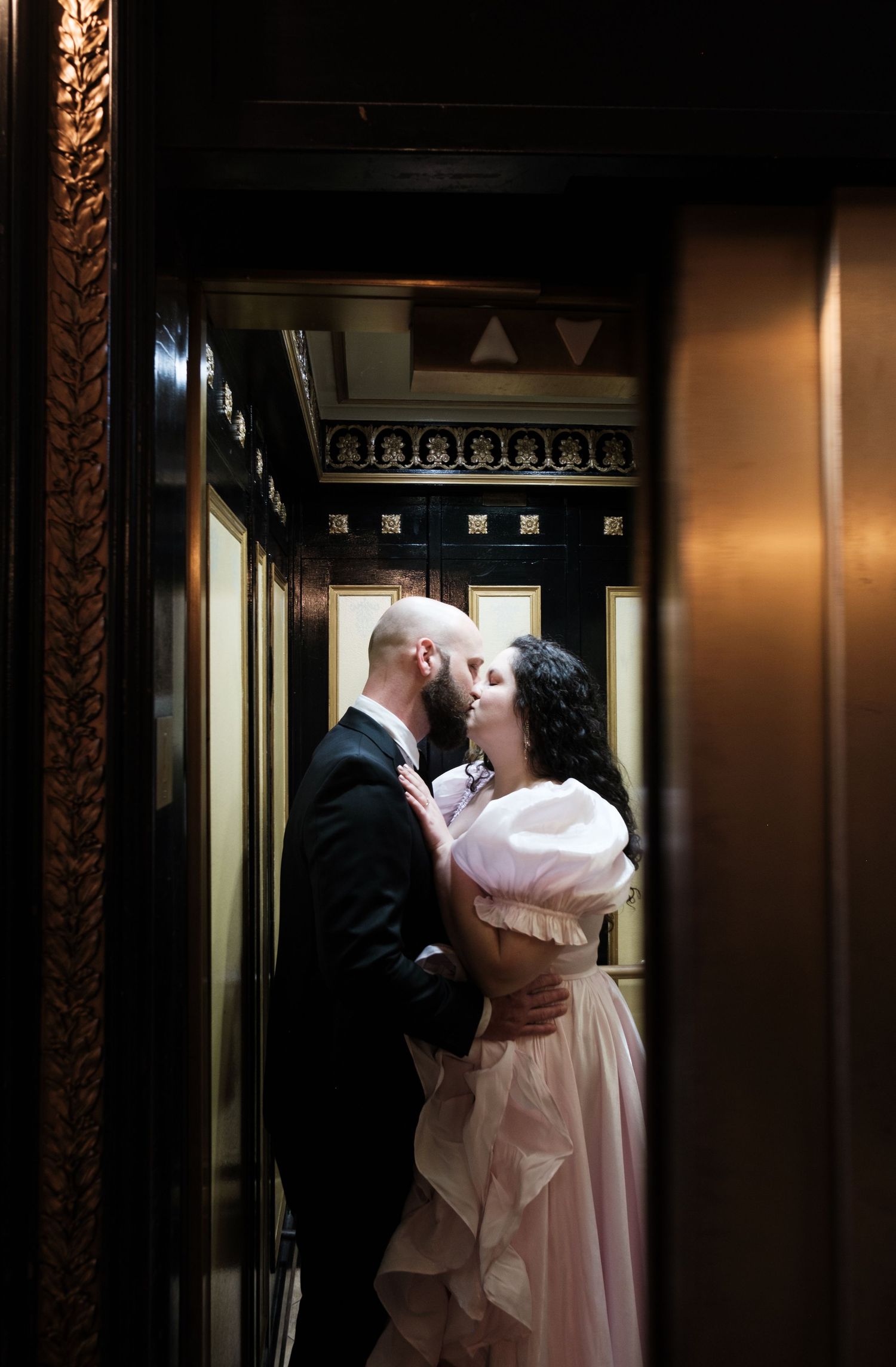Romantic couple embracing in dimly lit hallway with ornate framed walls.