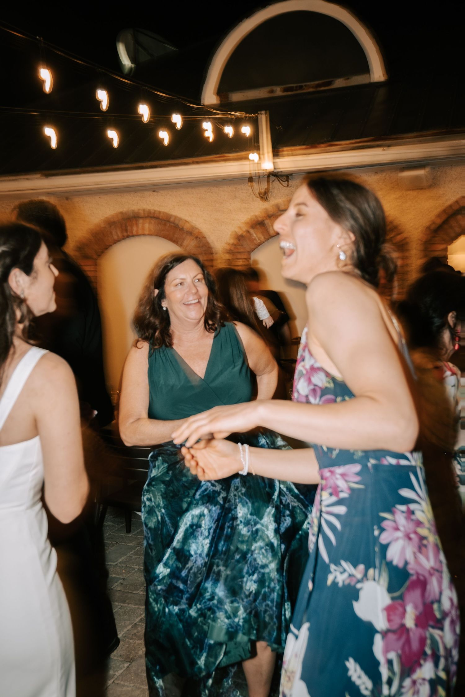 Wedding reception dance floor with guests dancing under string lights and arched doorways.