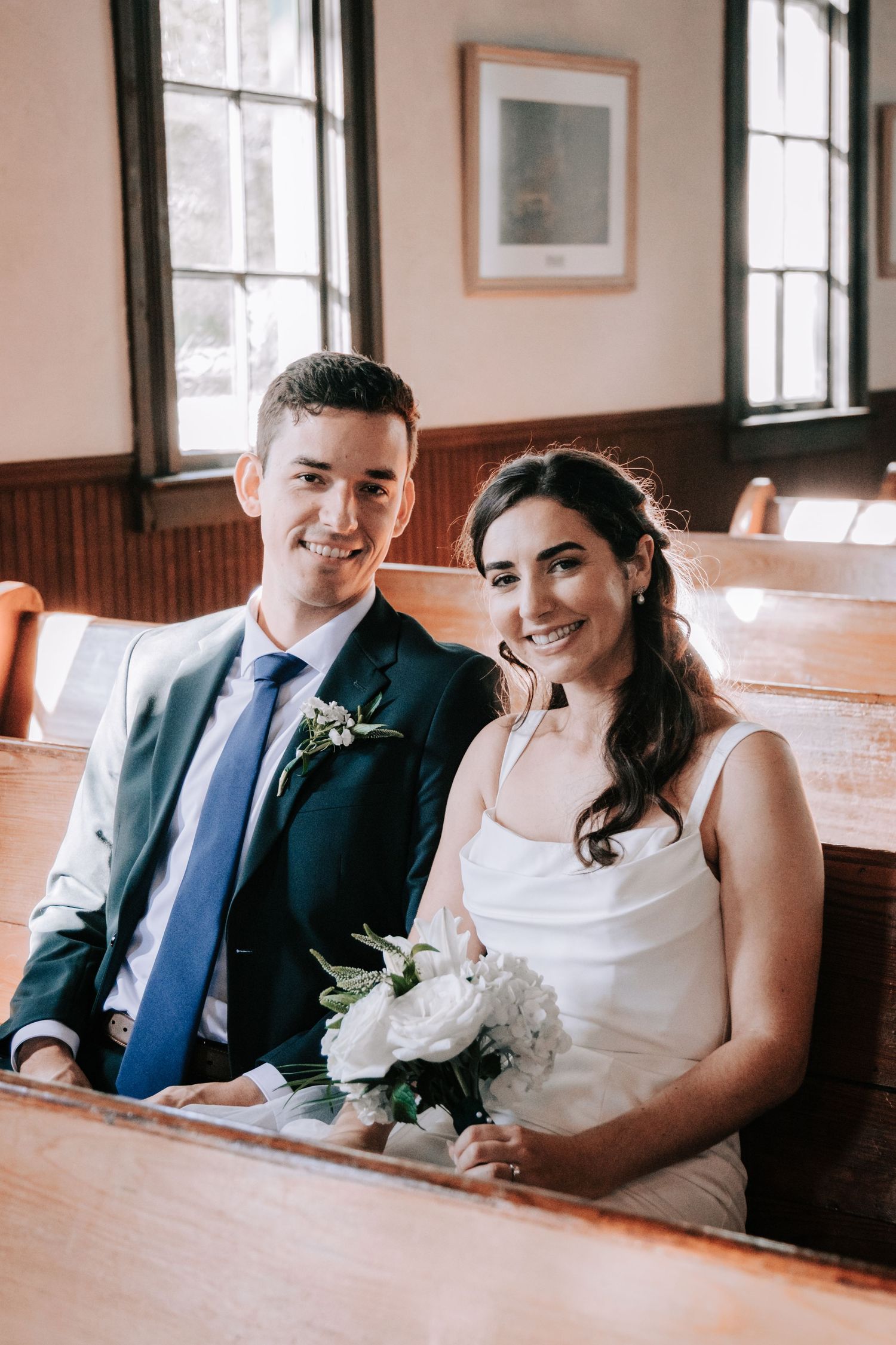 Newlywed couple shares intimate moments sitting together in wooden church pews during their wedding celebration.