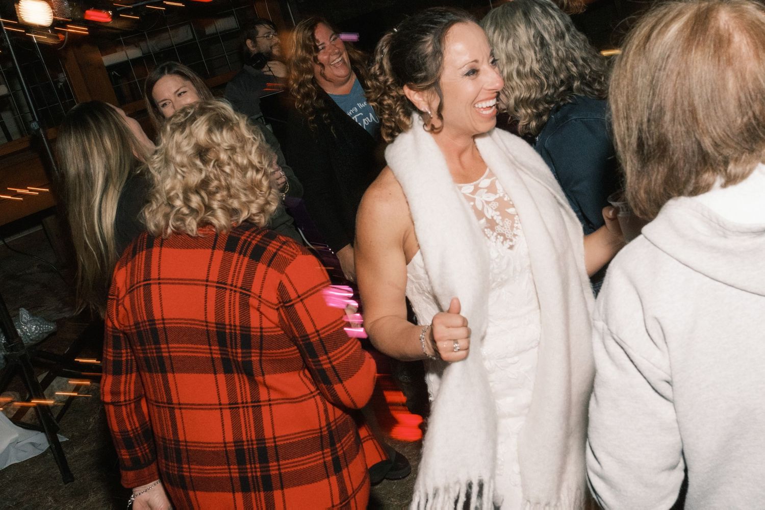 Bride in white lace dress with scarf dancing with guests at wedding reception.