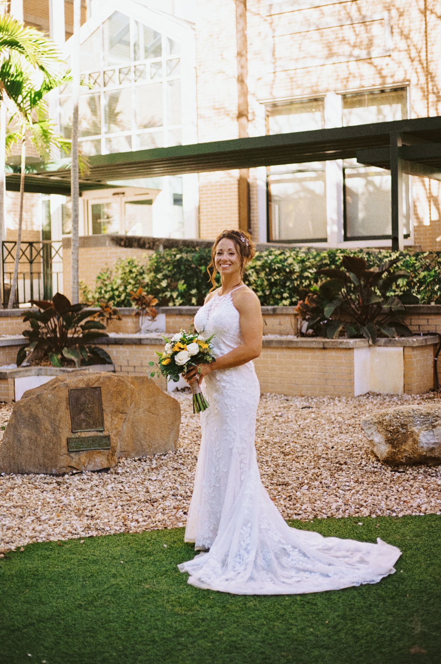 Bride in fitted lace gown holding bouquet posing in outdoor garden setting.