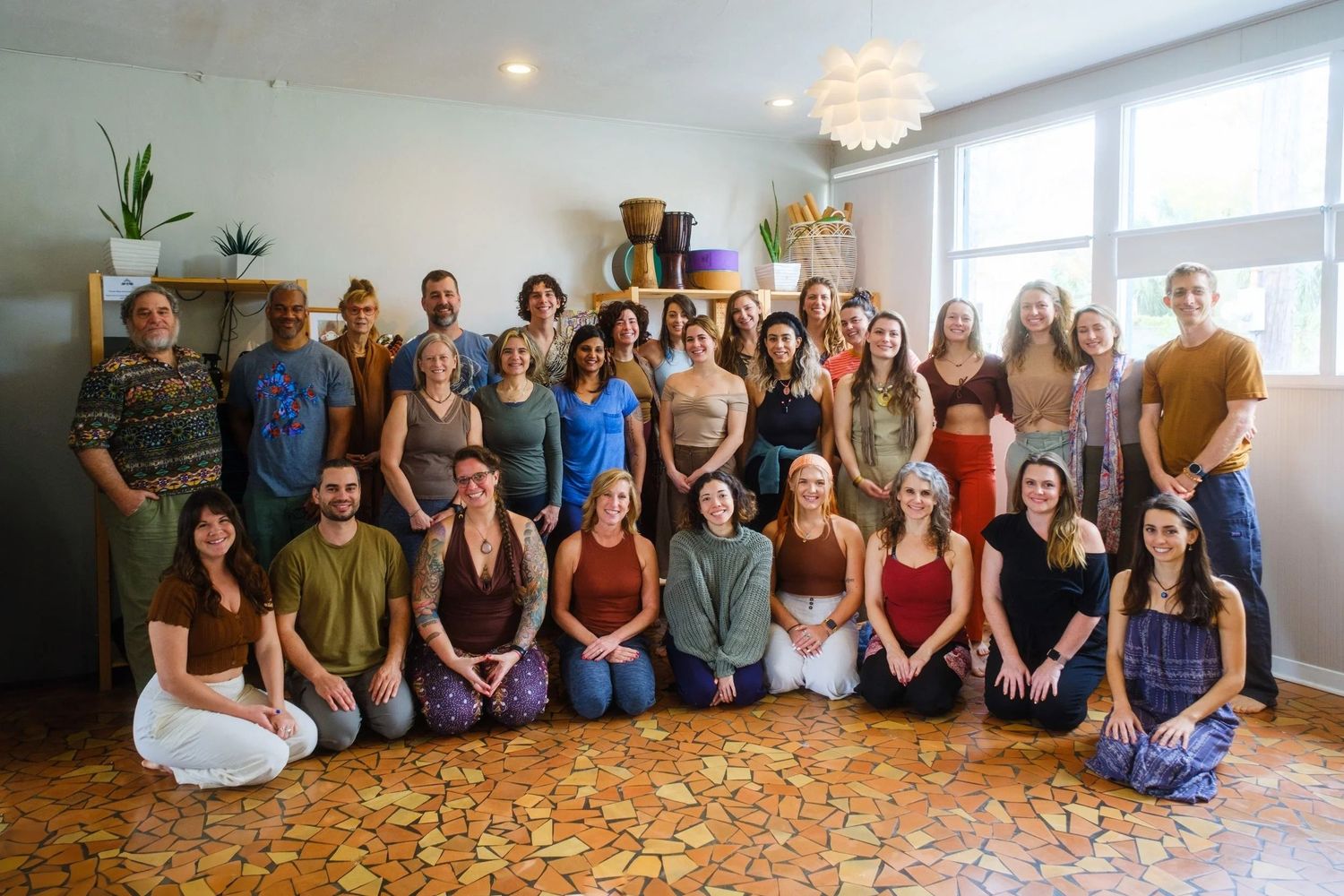 Large group photo of people sitting together in a bright indoor space with plants.