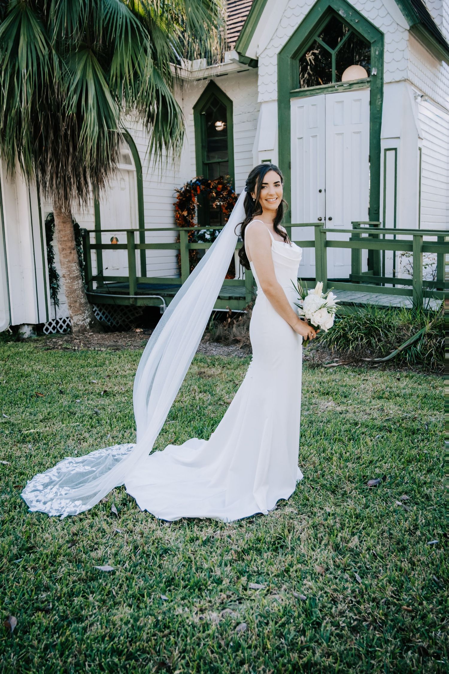White wedding dress flowing in the breeze against historic chapel buildings and palm trees.