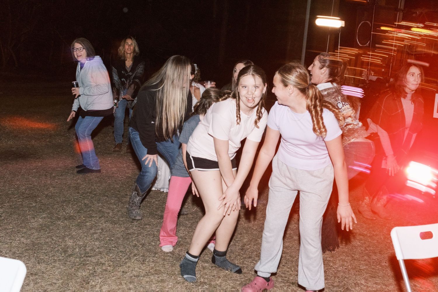 Group of young girls dancing and having fun outdoors at a nighttime wedding reception celebration.