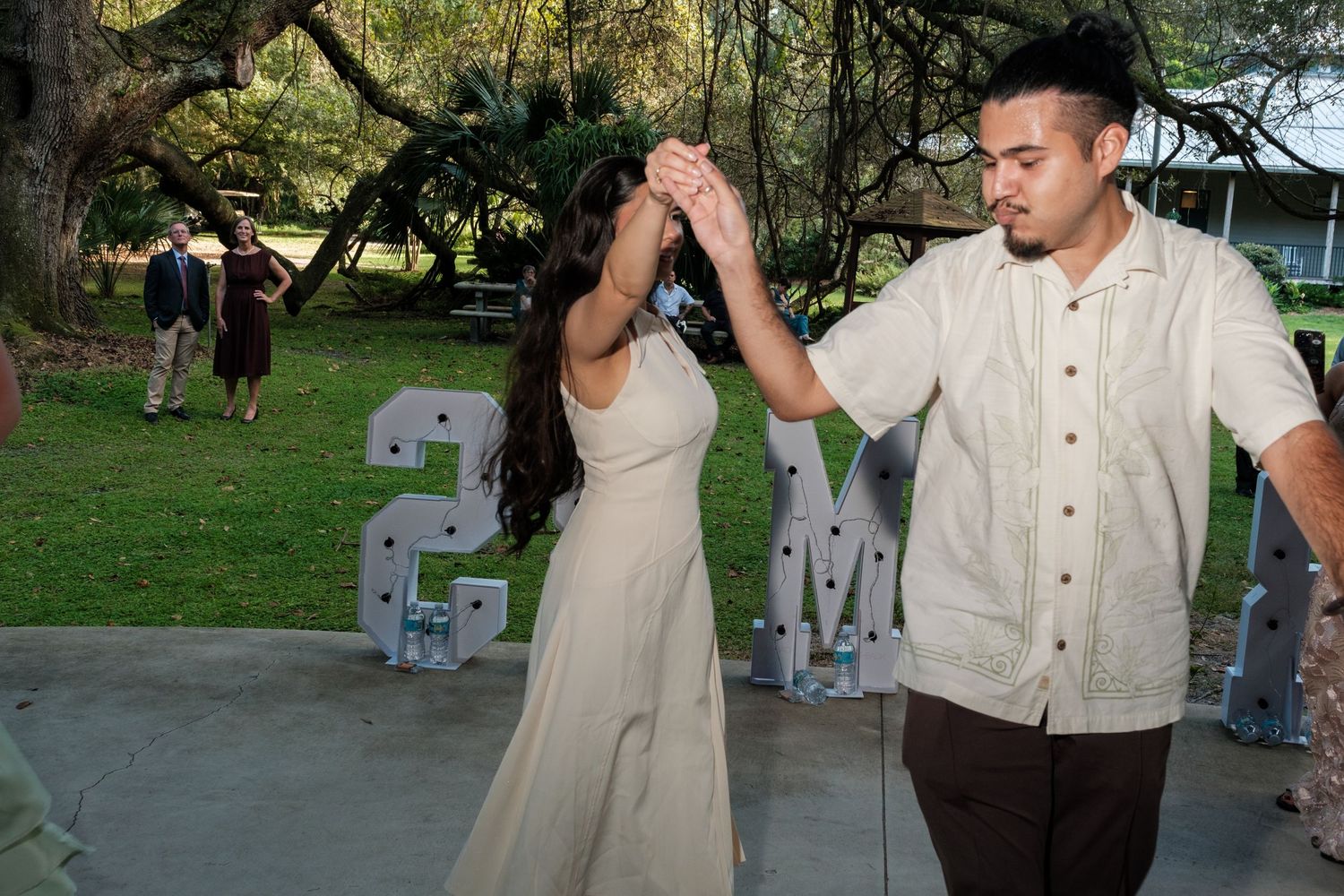 Wedding party dancing and celebrating outdoors with trees in the background.