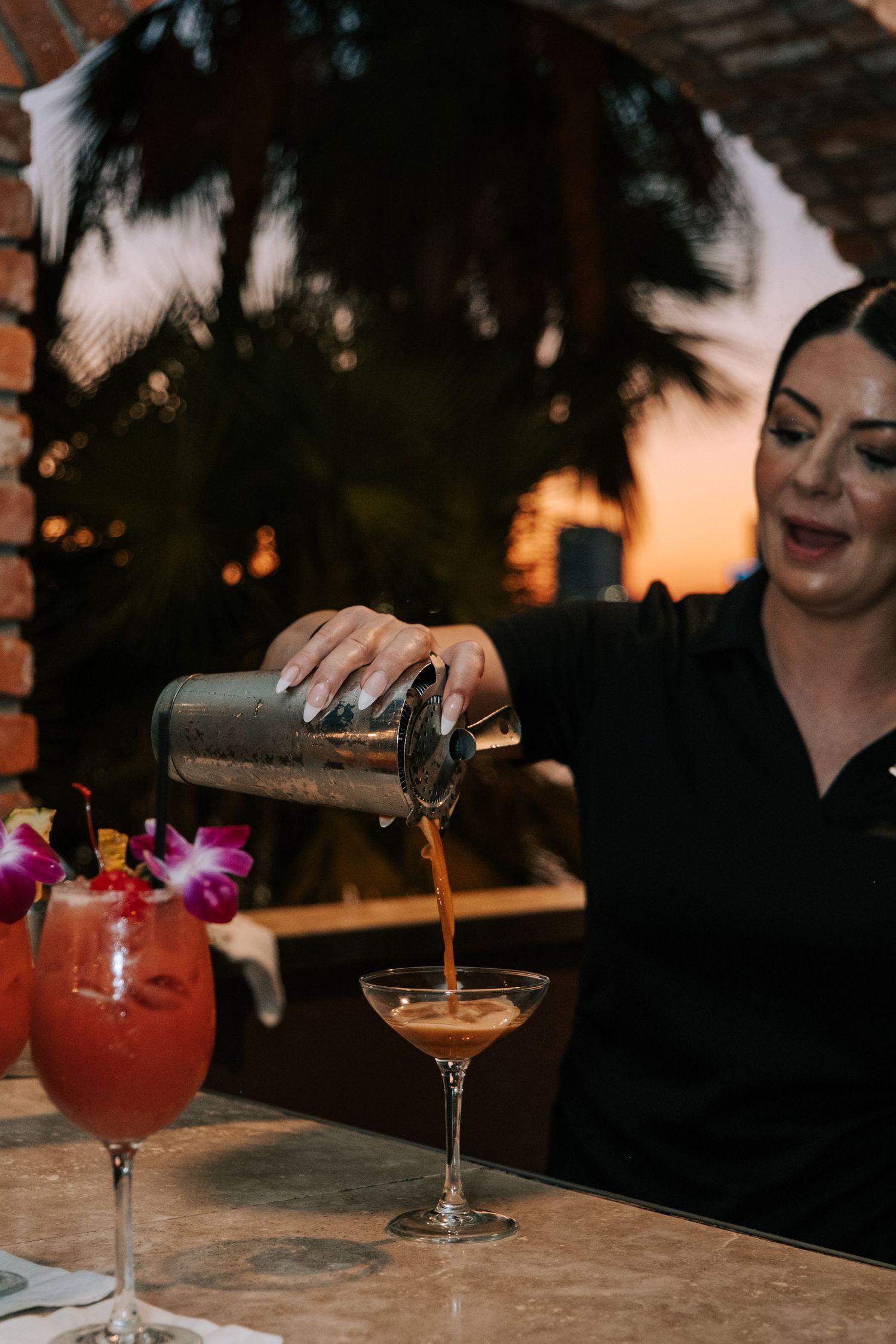 Colorful cocktails being poured at a wedding reception bar with tropical garnishes.