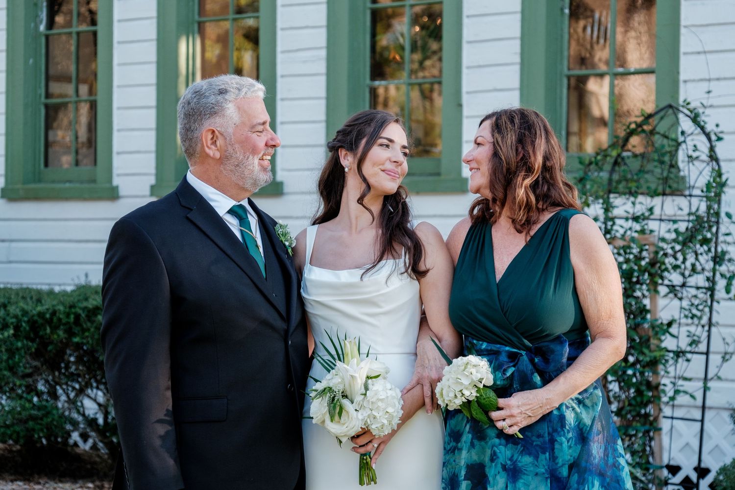 Wedding party gathered outside a white church with green trim on a sunny day.