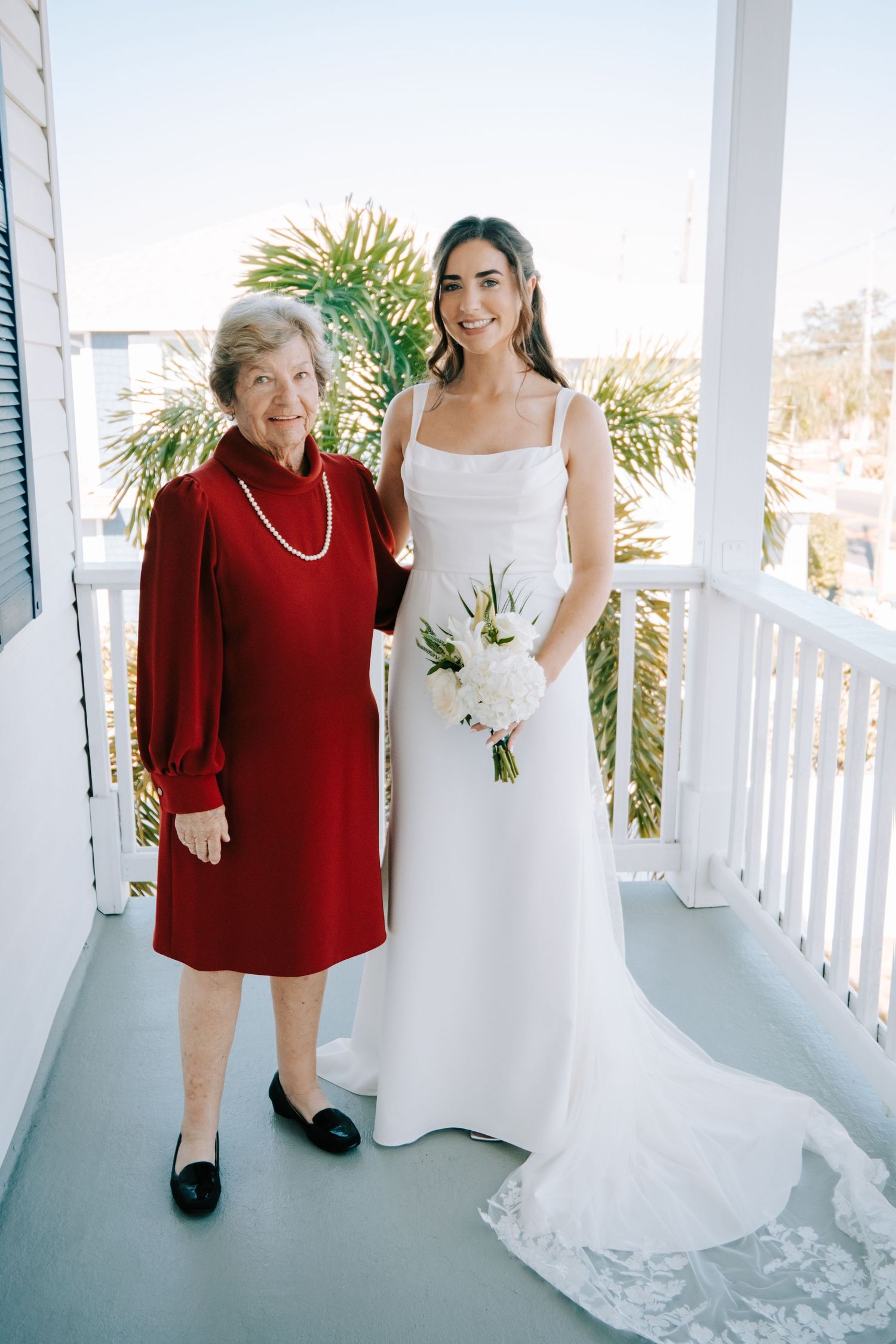 Wedding photos on a white porch showing tender moments between bride and companion in red.