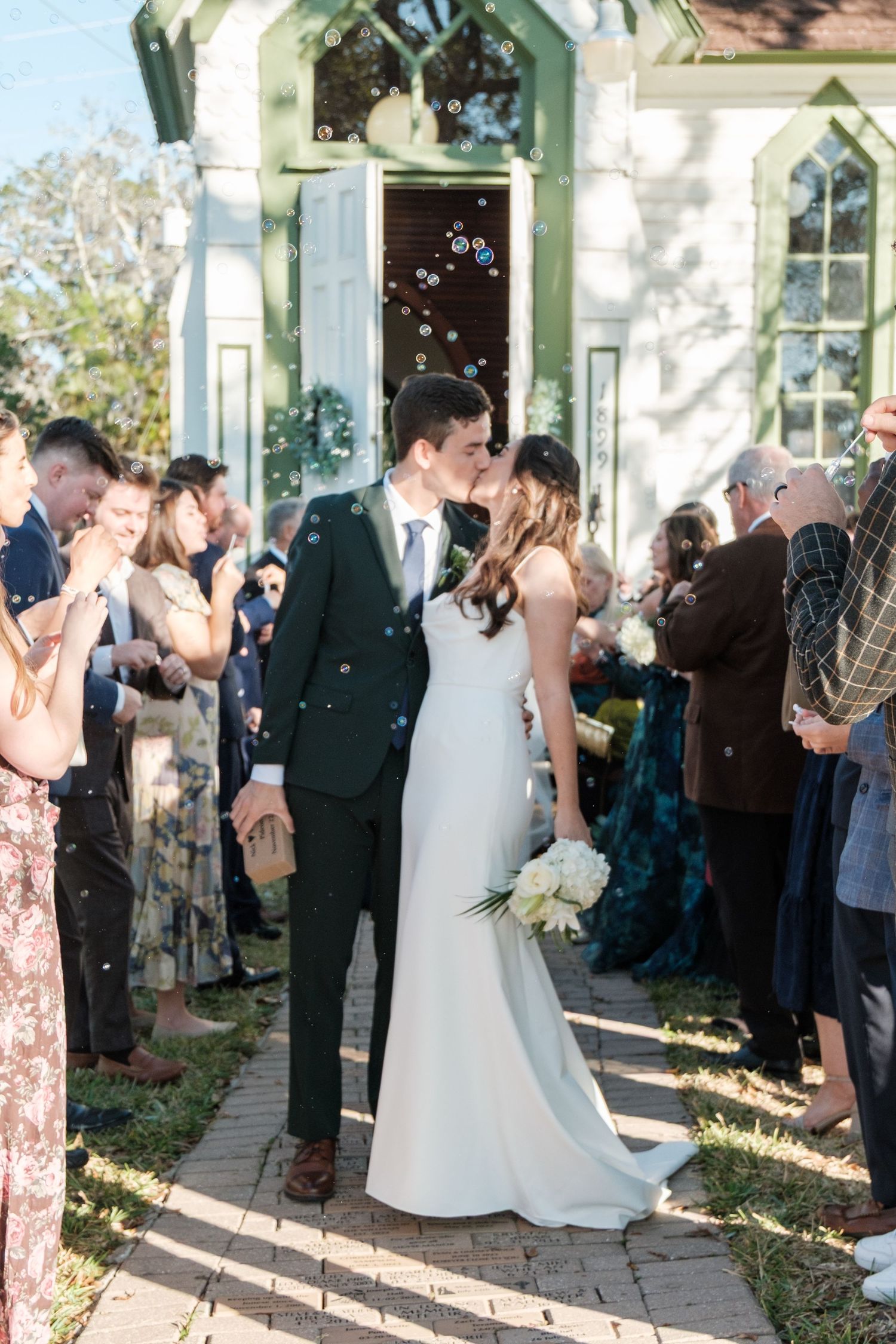 Wedding guests line up outside a white building to celebrate the newlyweds.