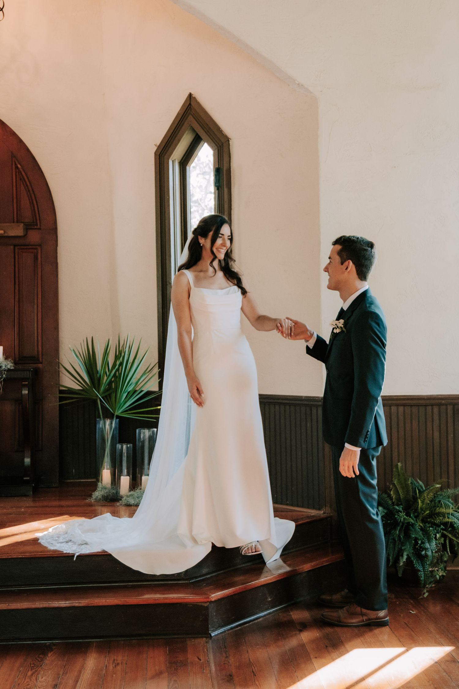 A wedding scene in a sunlit chapel with elegant architectural details and wooden floors.