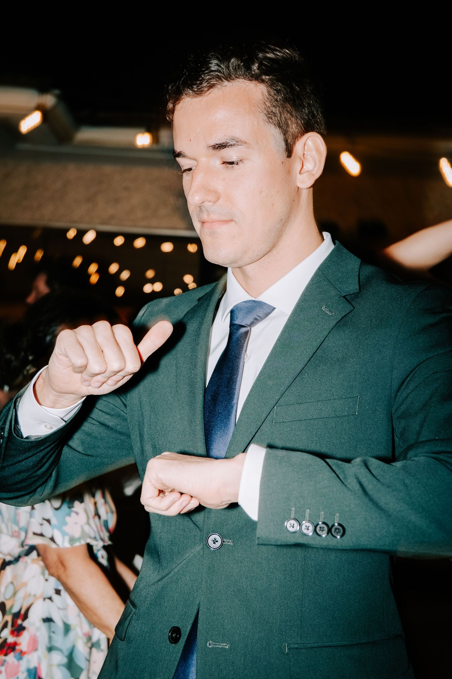 Groomsman in dark suit performing dance moves at wedding reception.